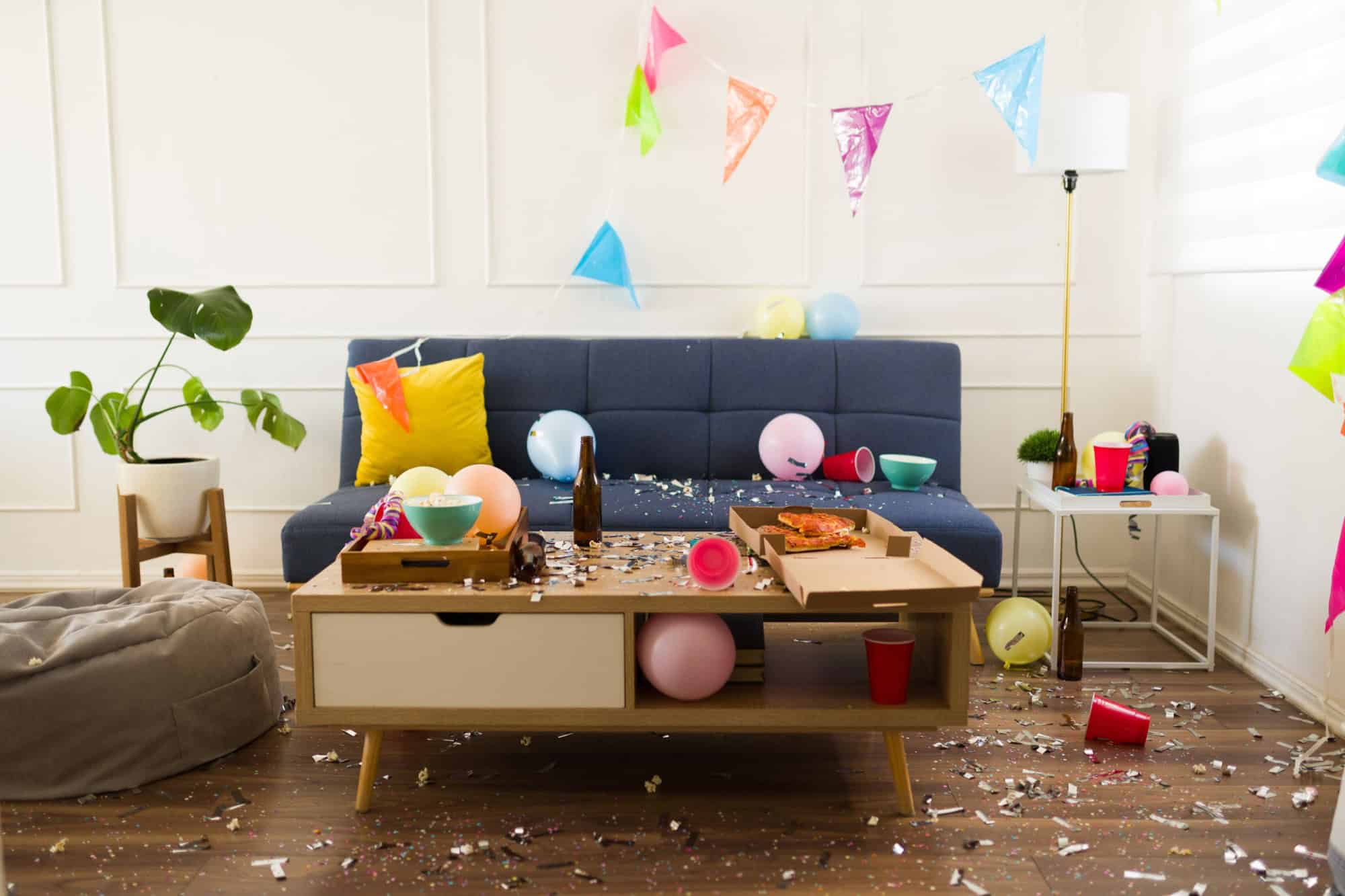 Living room home with confetti, balloons and party decorations having a disaster with trash and a mess after celebrating a birthday party 