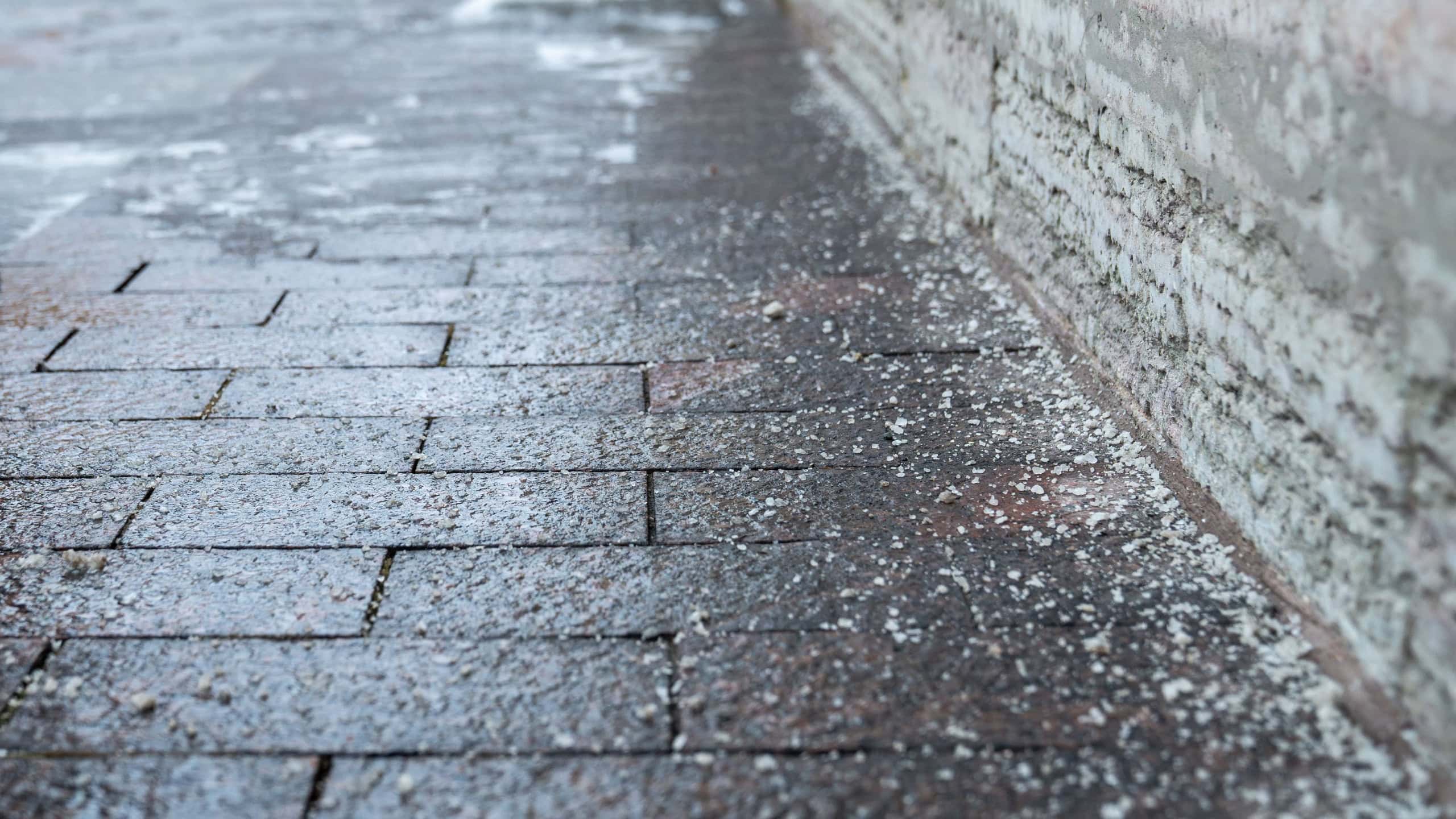 Deicing chemicals on pavement in winter. Salt grains on icy sidewalk, paving slab with rock salt in cold season. Slippery road sprinkled with technical salt and calcium.