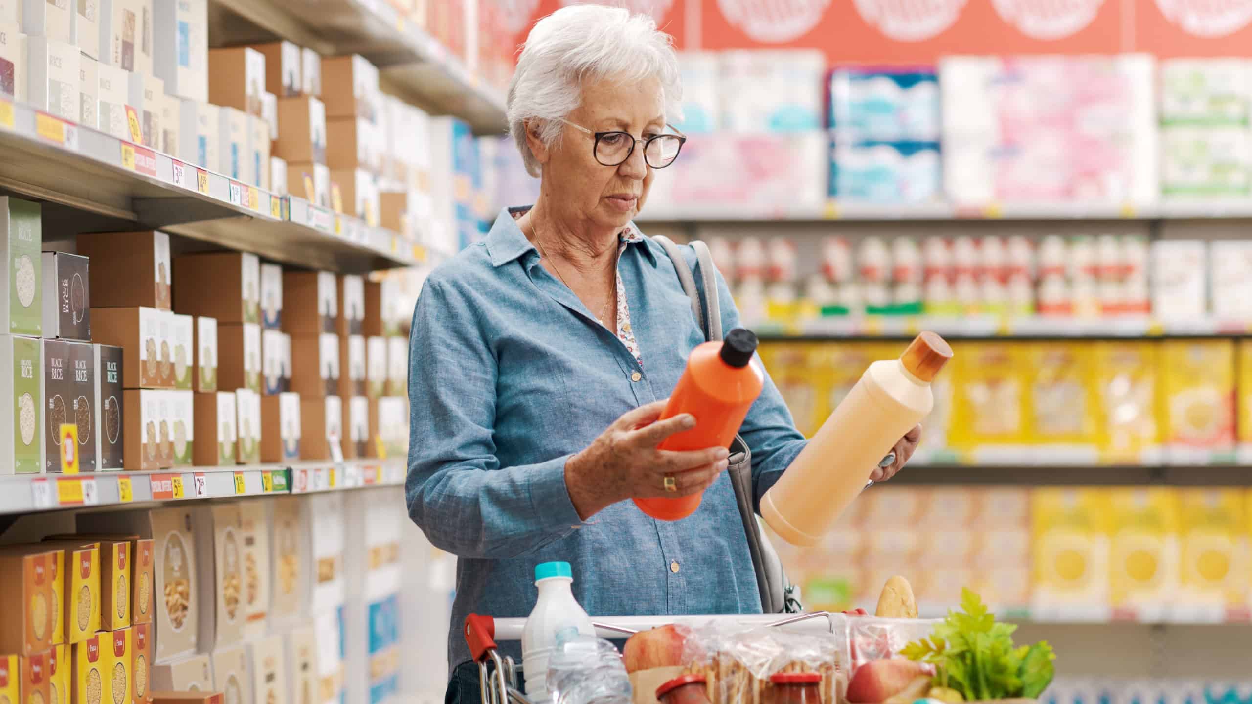 Senior customer buying groceries at the supermarket, she is holding two bottles of detergents and comparing products