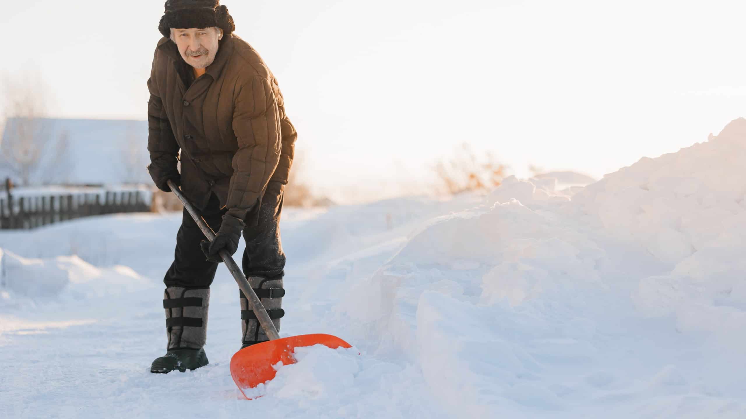 Elderly man cleaning snow with shovel after snowstorm, sunlight.