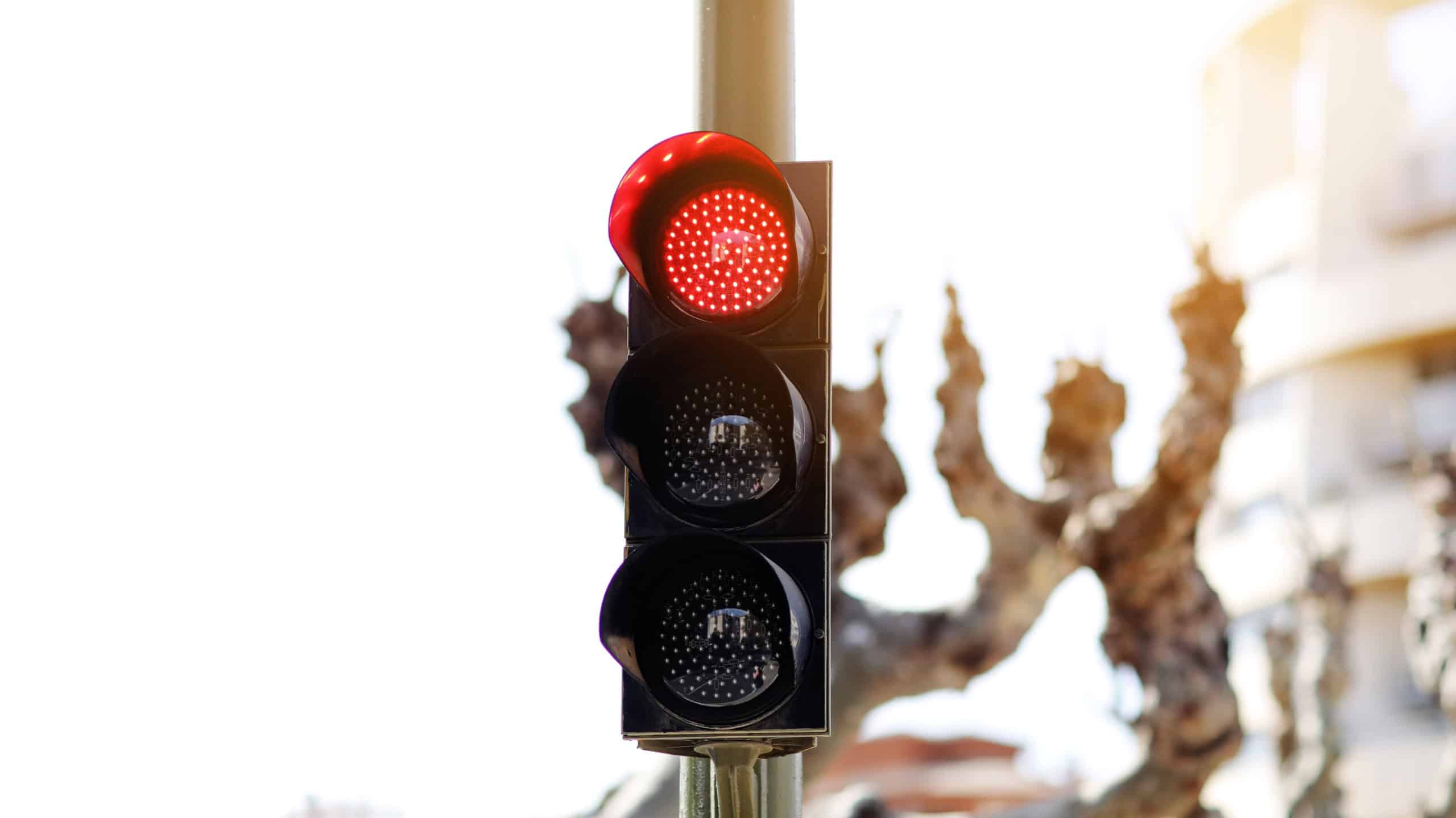 LED red light traffic light on defocused european buildings and trees background. City crossing with red light in semaphore, traffic control and regulation concept. Valencia, Spain.