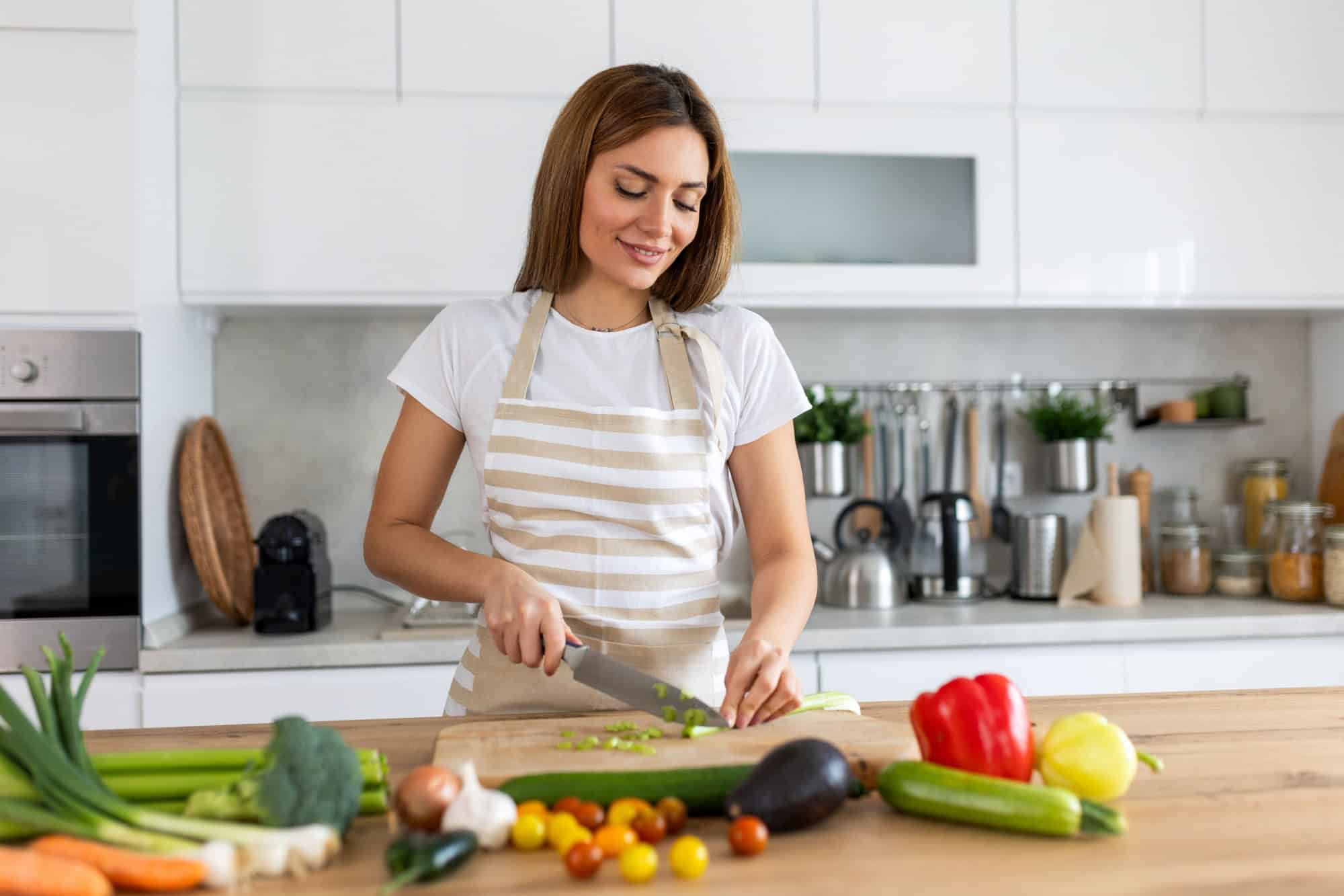 Beautiful young woman stand at modern kitchen chop vegetables prepare fresh vegetable salad for dinner or lunch, young woman cooking at home make breakfast follow healthy diet, vegetarian concept