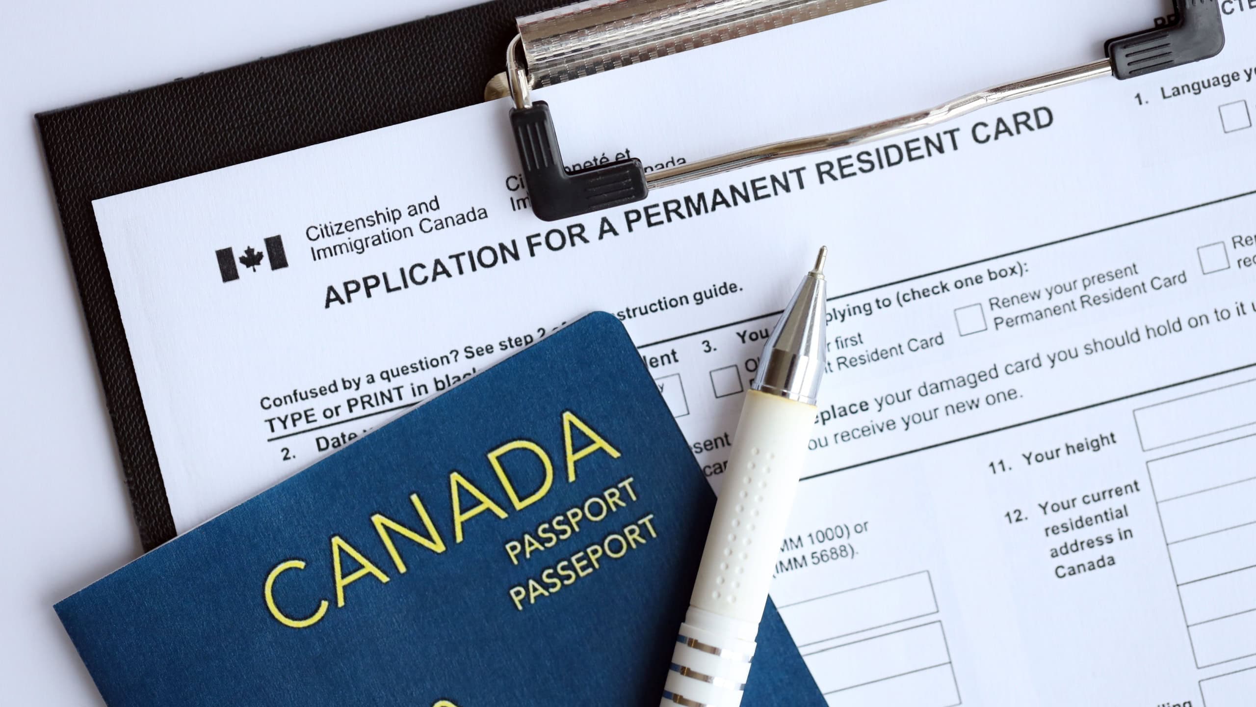 Application for permanent resident card on table with pen and canadian passport close up