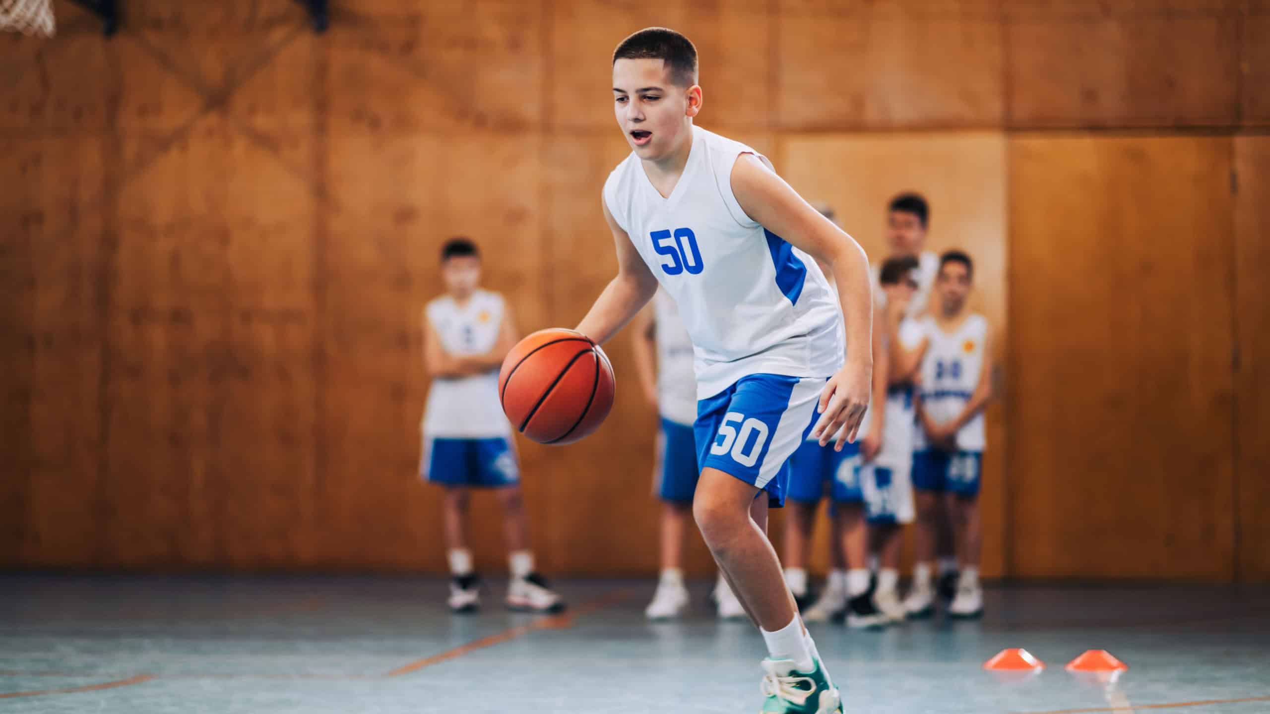 Full length of a junior basketball player in action dribbling a ball on training at court. A young athlete in motion practicing basketball while dribbling a ball on court. A sporty kid with basketball