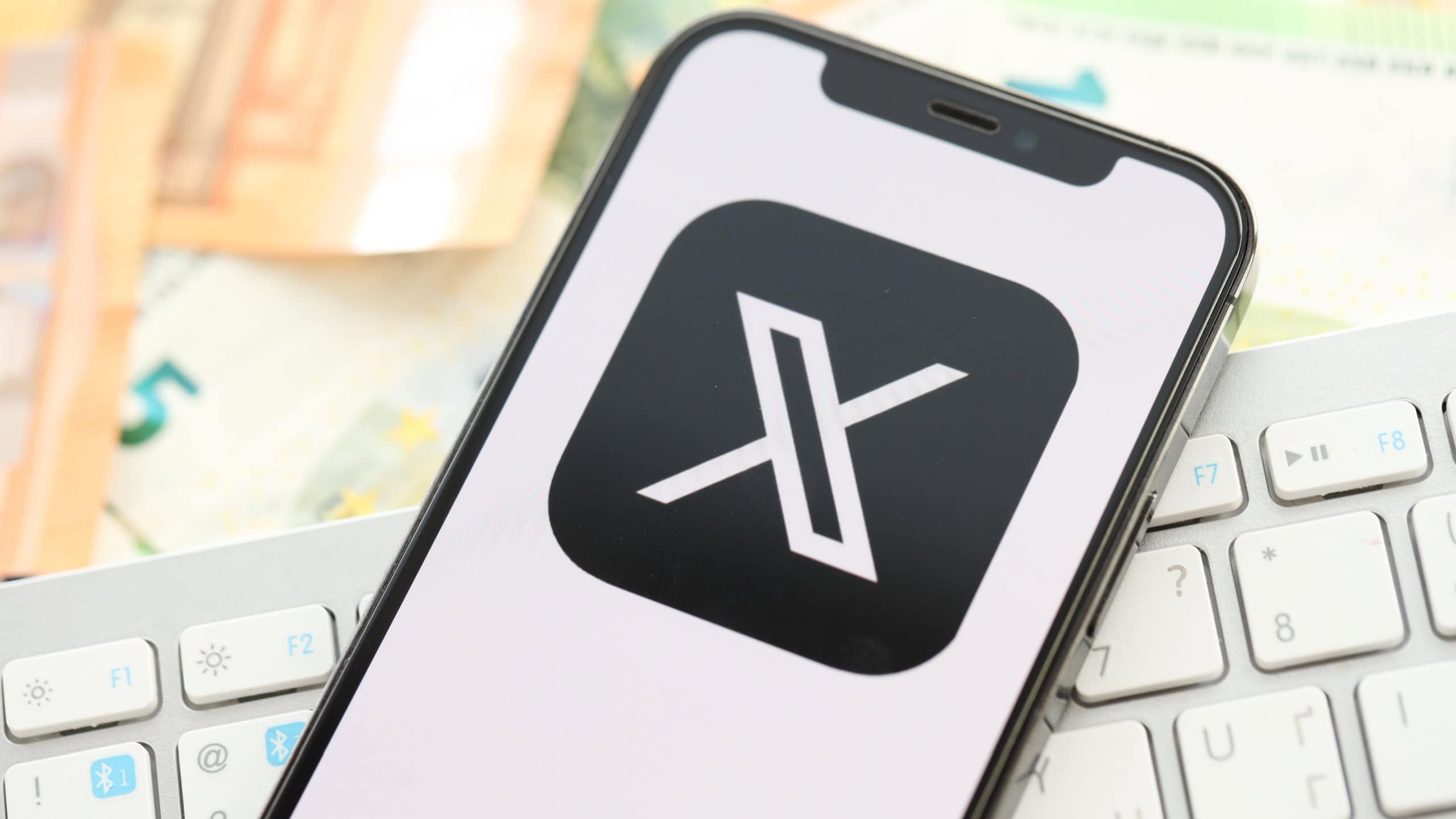 Twitter X icon on smartphone screen on many euro money bills. iPhone display with app logo with european currency euro banknotes and white keyboard
