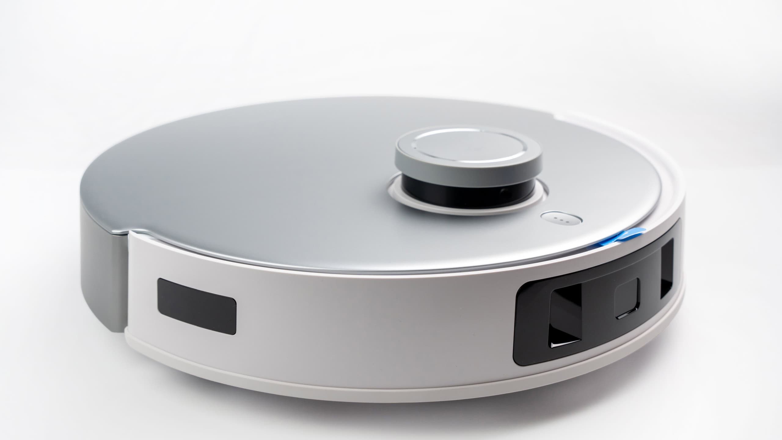 A robot vacuum cleaner with a round body and a silver and black color. The robot is on a white background