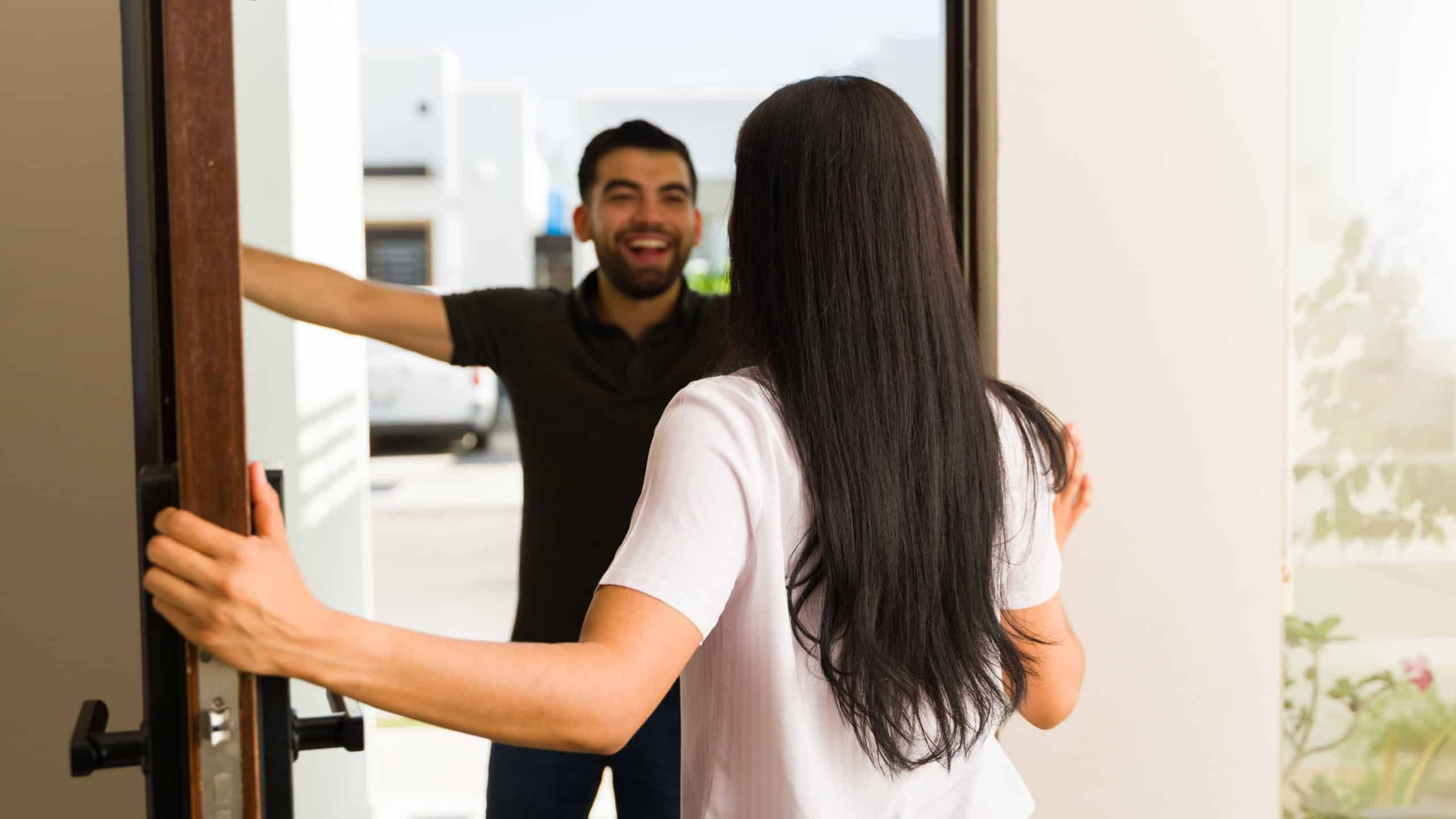 Happy latin woman is opening the door to her male friend who is arriving at her home for a visit