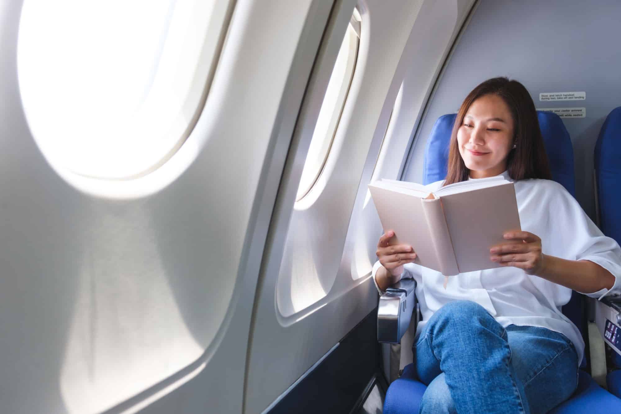 Portrait image of a woman reading book while traveling on an airplane