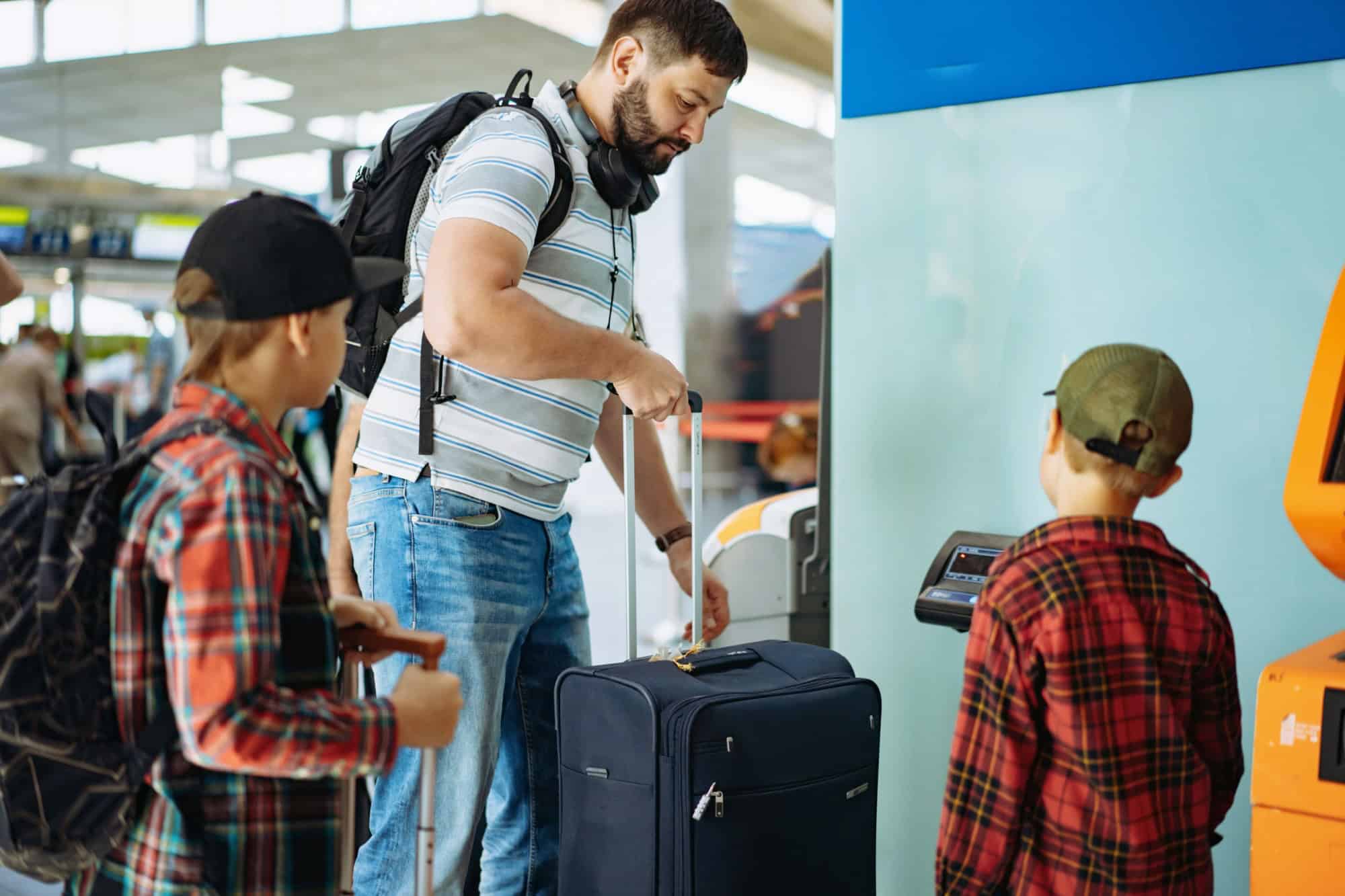 caucasian bearded man with children in airport putting suitcase on weights mesuring luggage