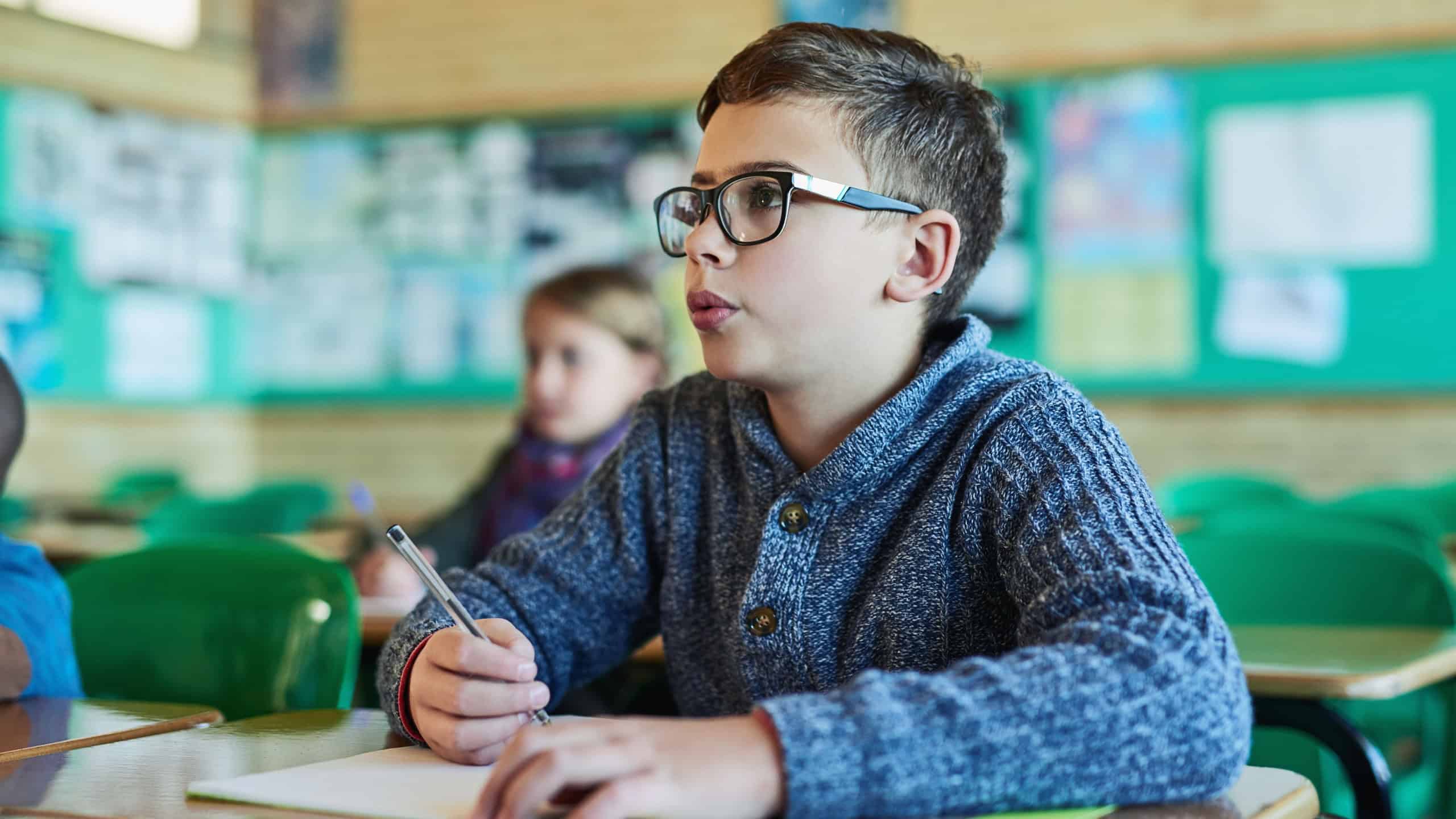 Boy, child and writing with book in classroom for learning, listen and development for education. Kid, notebook and thinking with information, scholarship and study with progress for future at school