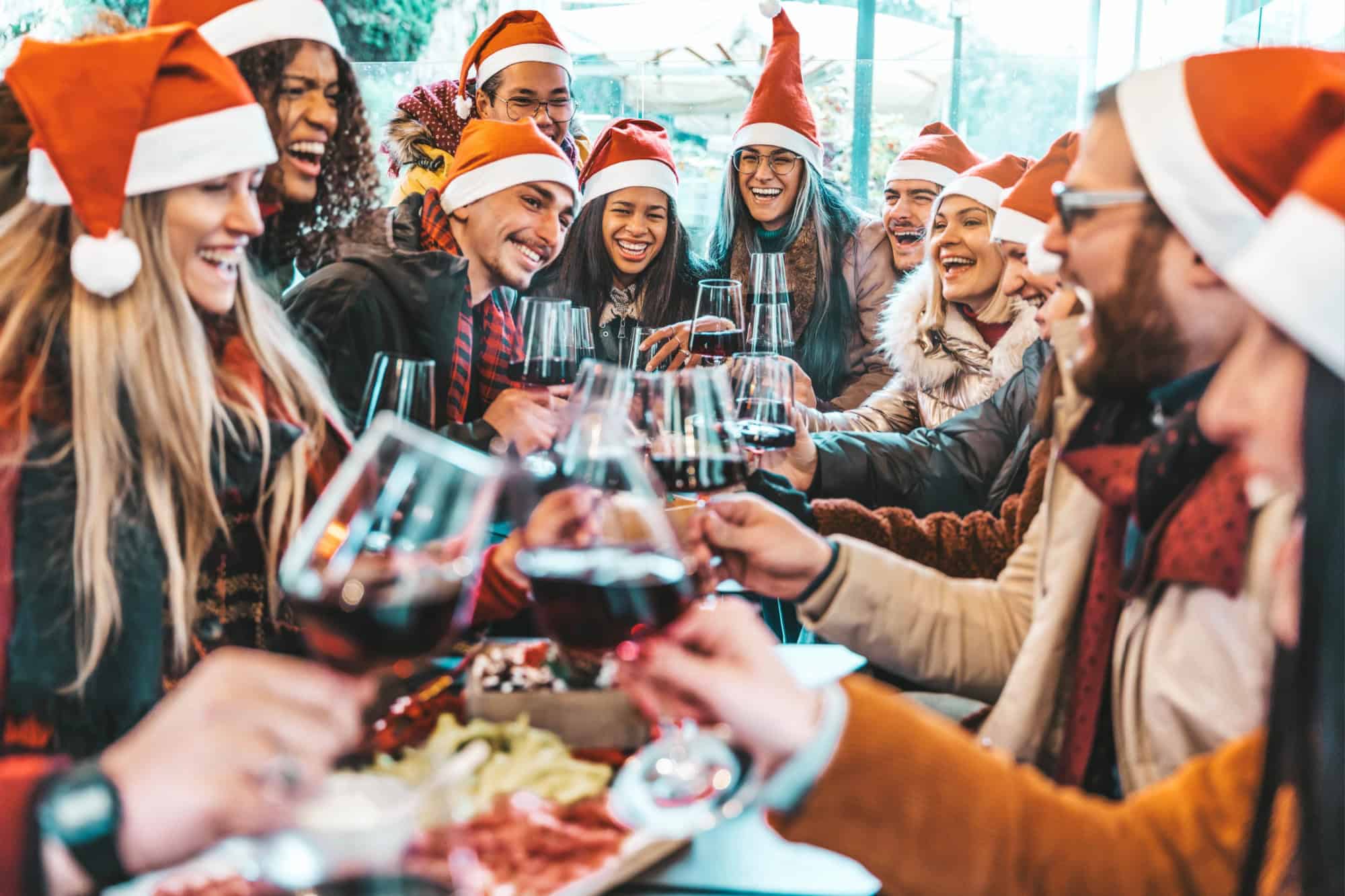 Happy people wearing santa claus hat having Christmas dinner party - Cheerful group of friends celebrating new year together - Winter holidays concept