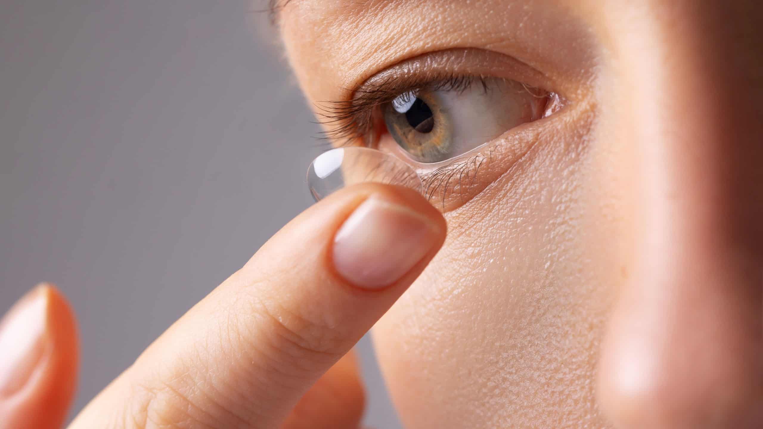 Young woman puts contact lens in her eye over white background. Eyewear, eyesight and vision, eye care and health, ophthalmology and optometry concept.