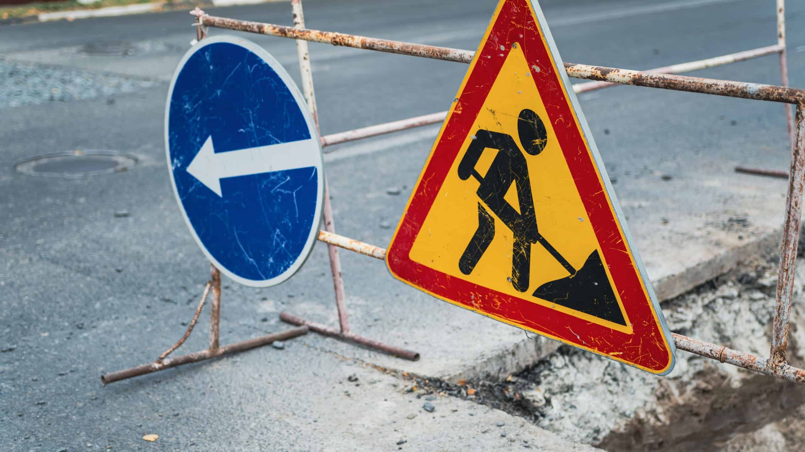 Roadwork in progress on a city street with safety barriers and construction signage indicating detour directions during daytime.