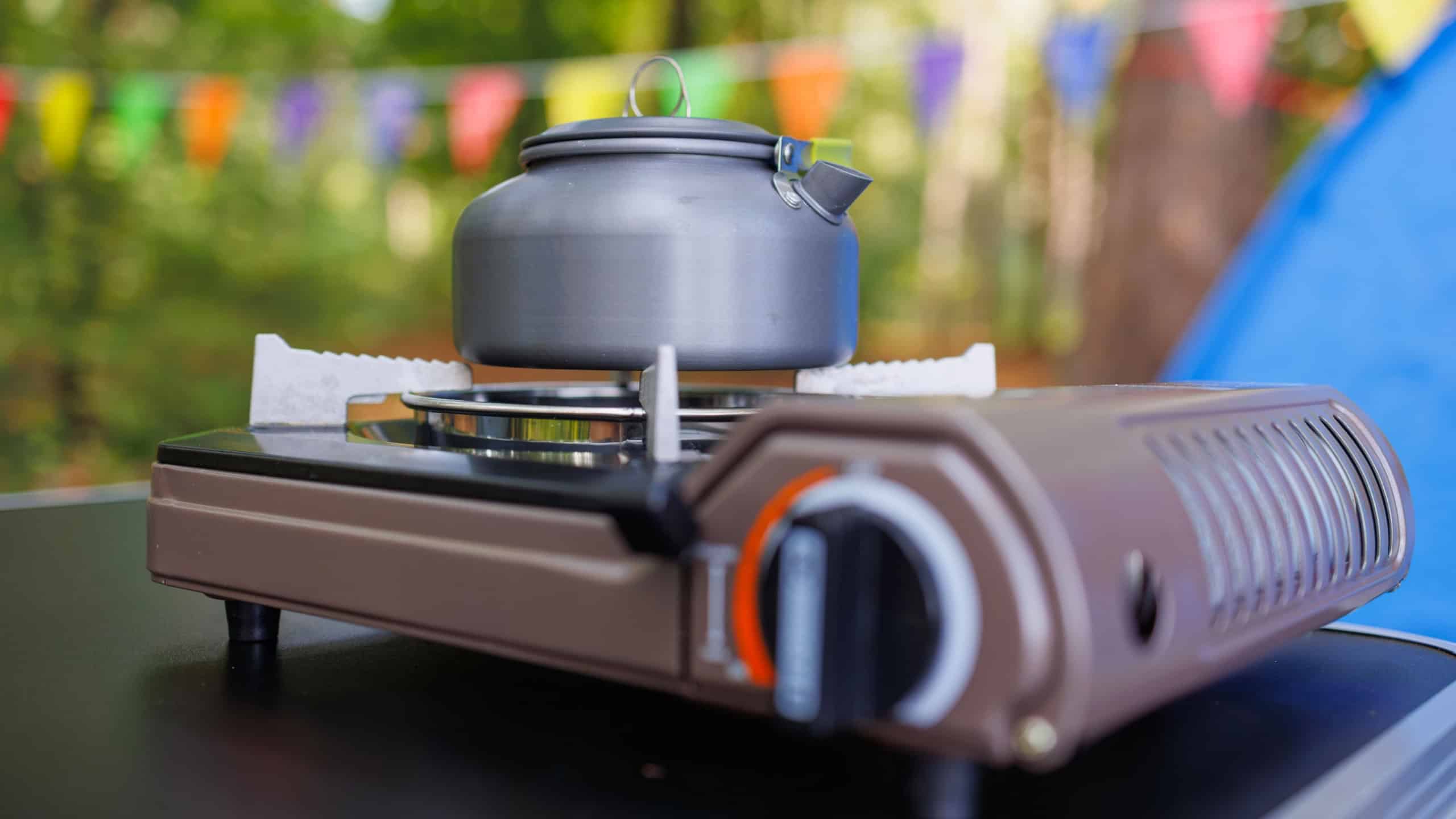 Camping kettle standing on a gas tourist stove against the background of a tent and carnival garlands in the forest