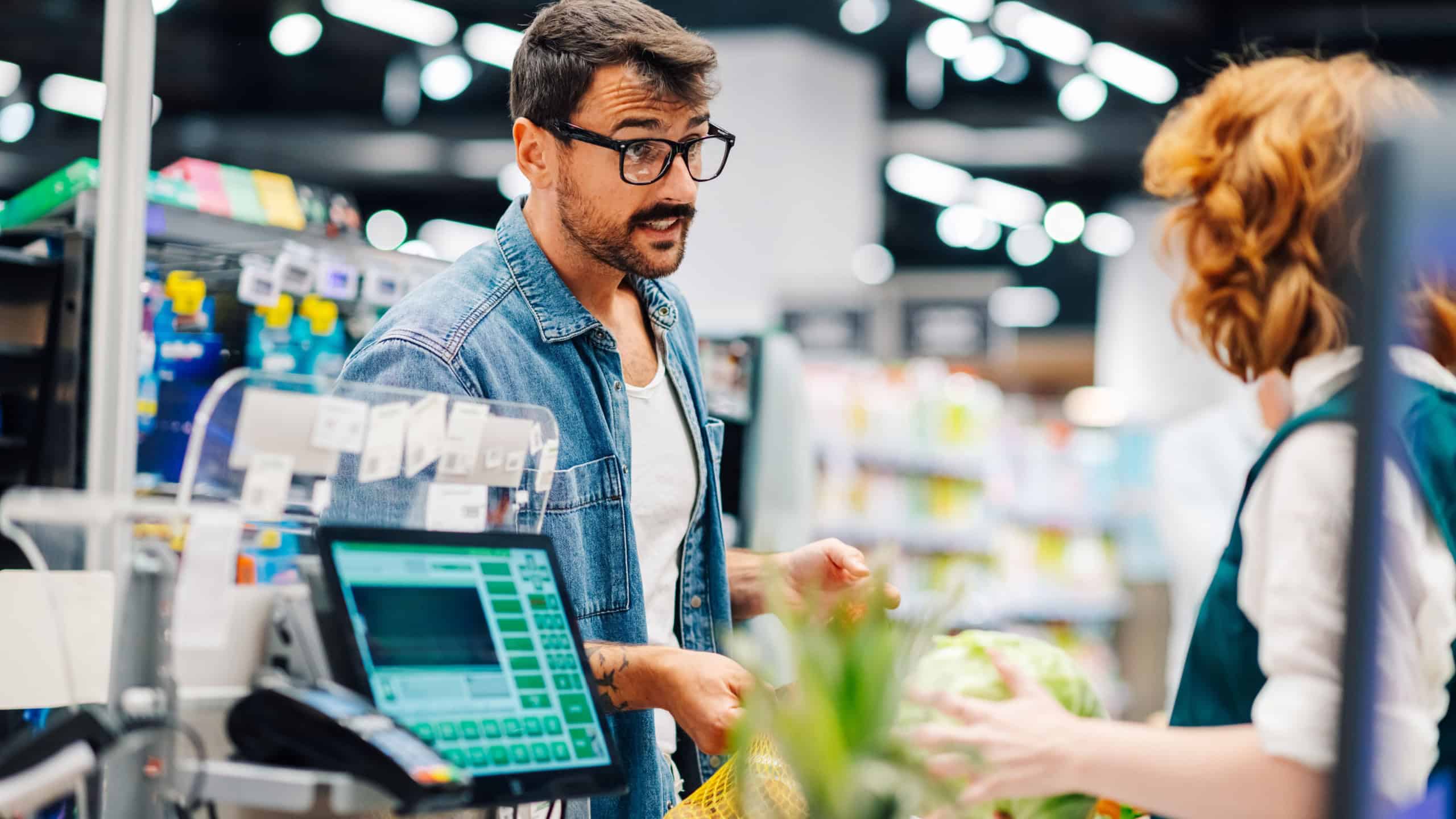 Frustrated customer at supermarket checkout expressing concerns to cashier with reusable bag. Modern interaction highlights sustainability and communication in retail