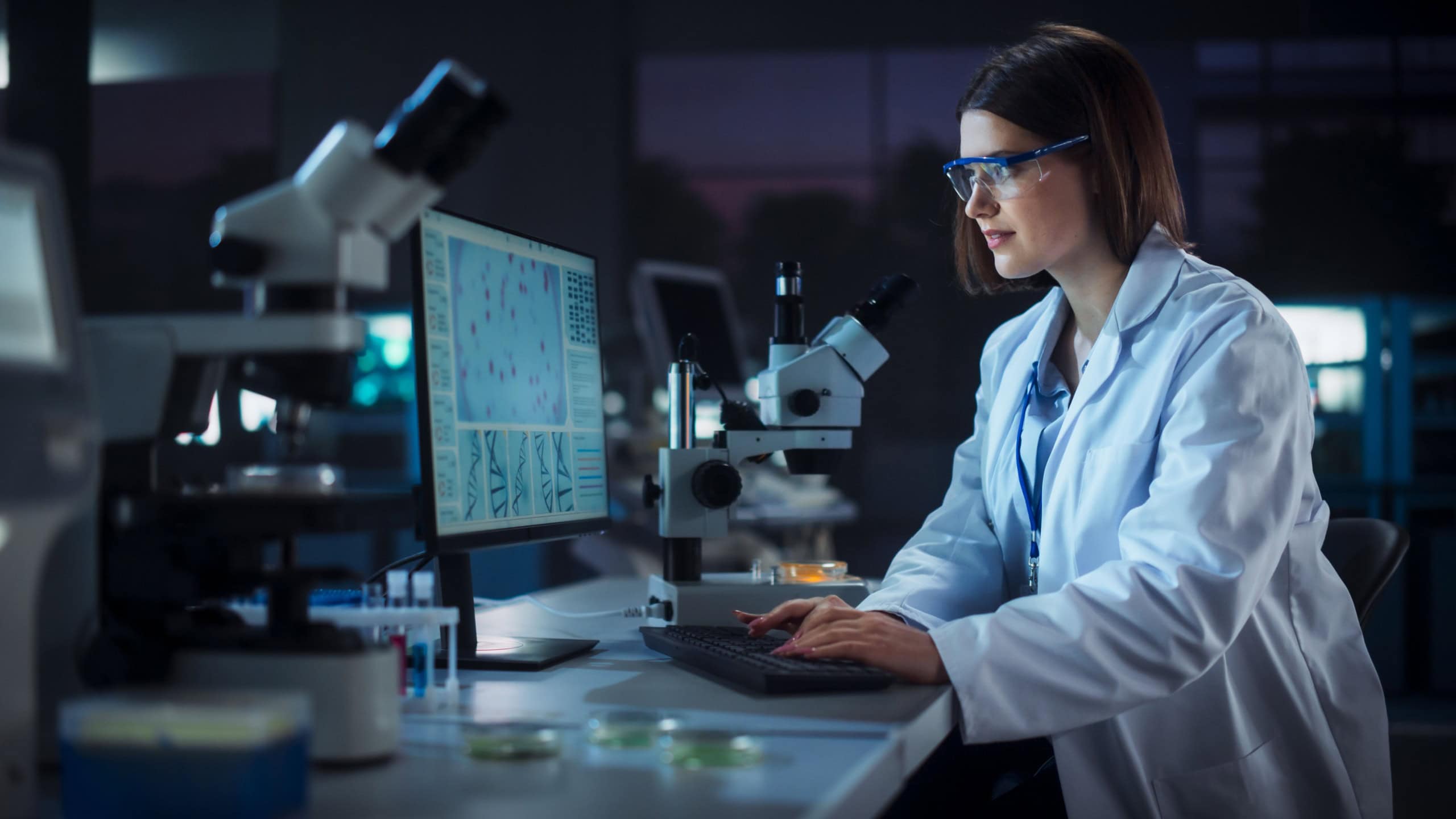 Caucasian Female Scientist Working on a Computer in the Evening. Specialist Using a Gene Sequencing Software. Advanced Biotechnology Lab in a Medical Research and Development Center
