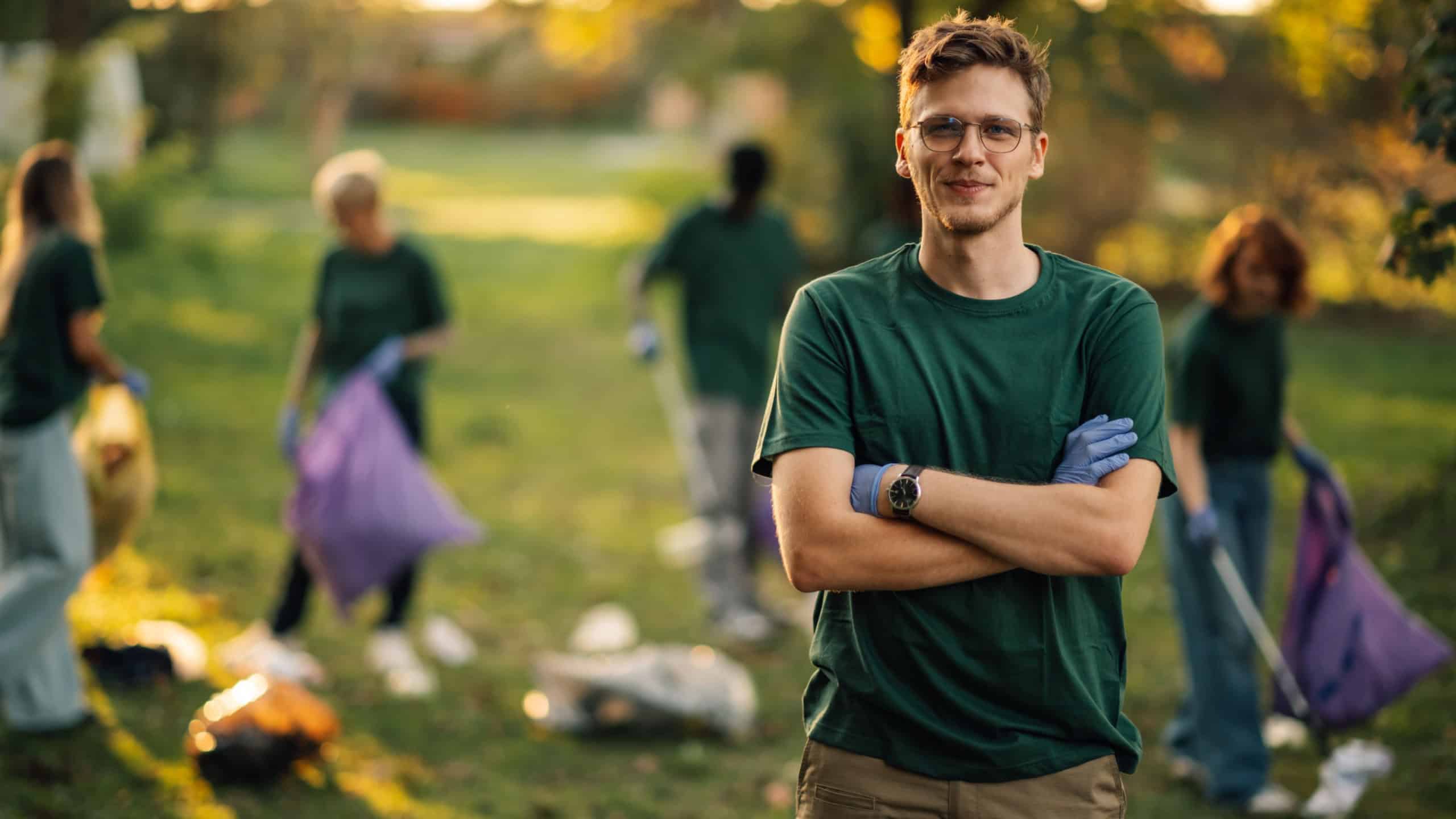 Confident young man volunteering to clean up garbage in a park with a team promoting sustainability and waste management. Together, they make a positive impact against pollution and climate change
