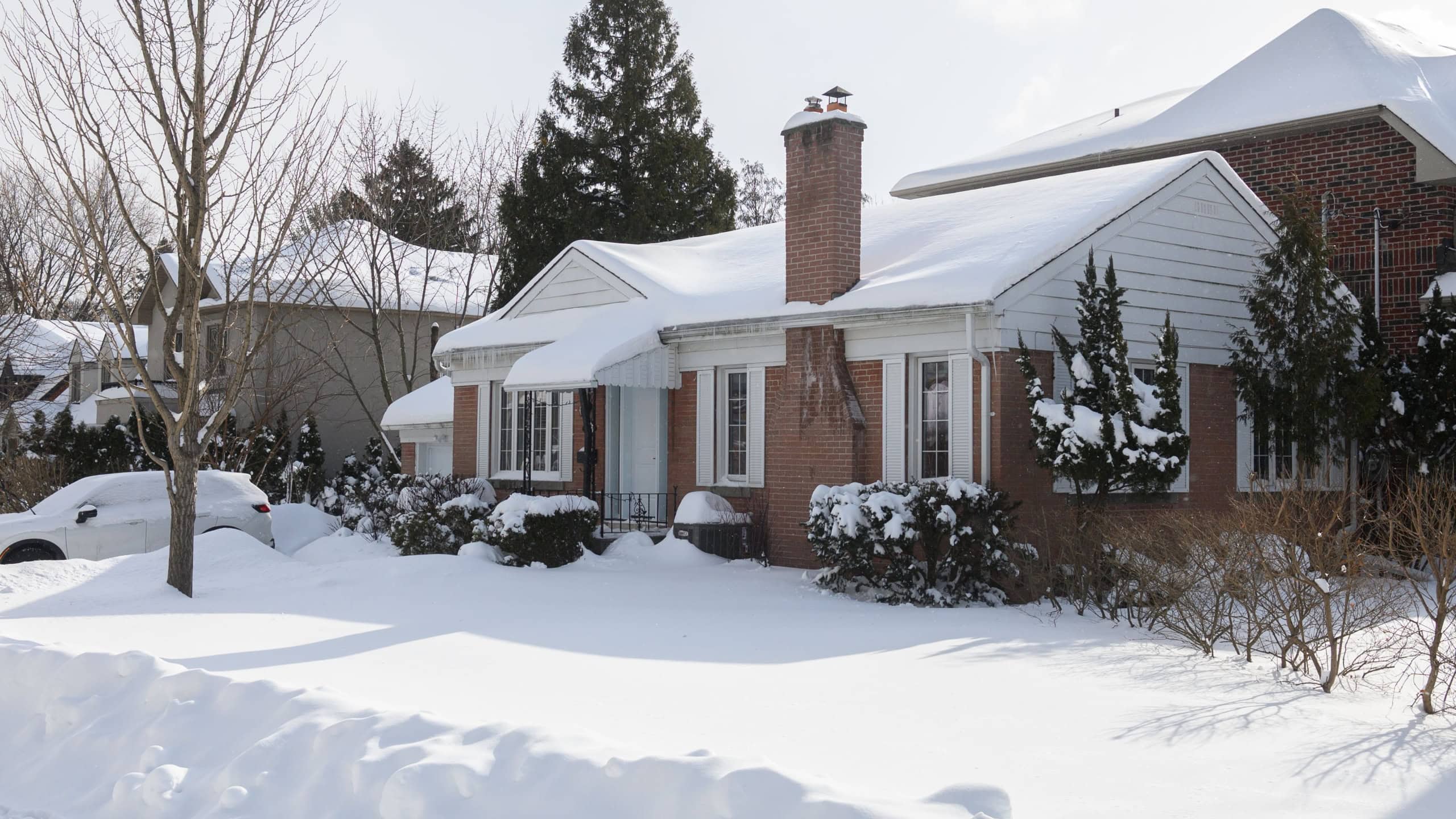 Toronto, ON, Canada - February 27, 2025: A suburban house stands covered in snow with icicles hanging from the roof, while the sunlight casts shadows on the white winter landscape.