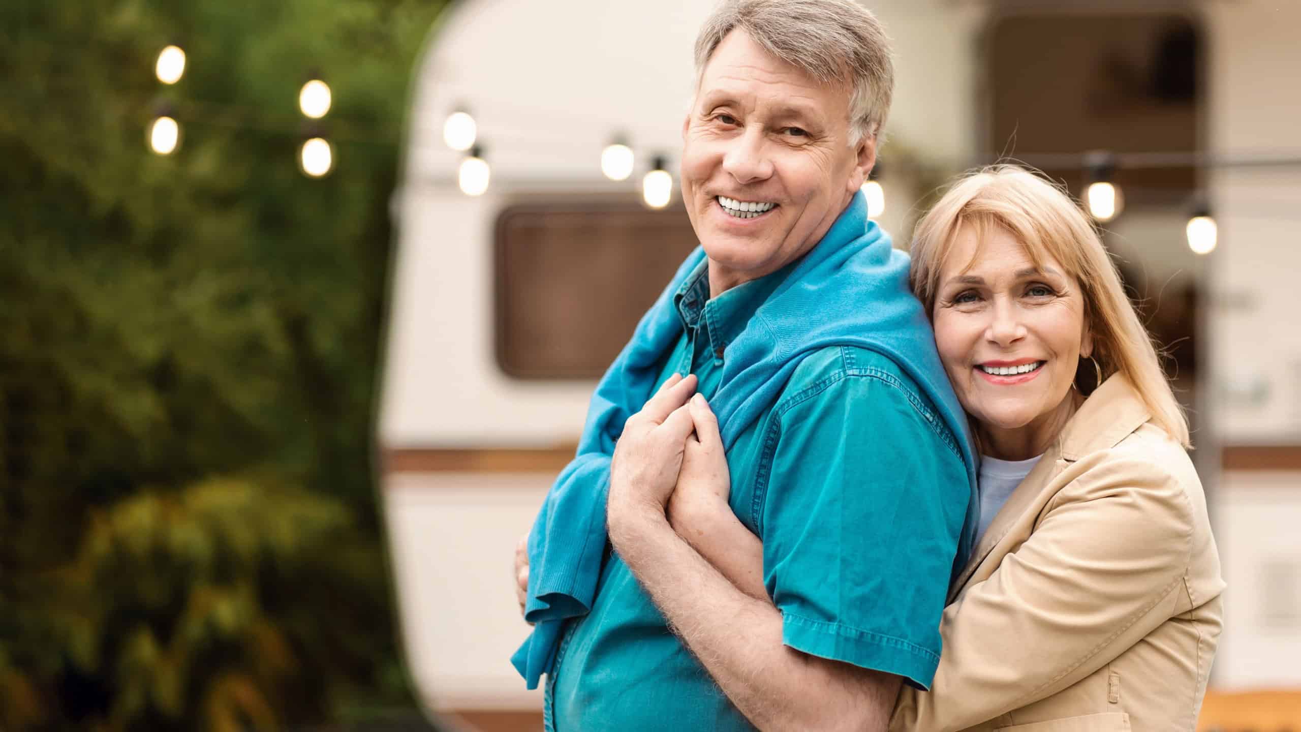 Camping together. Happy mature couple hugging each other on family vacation near their trailer.