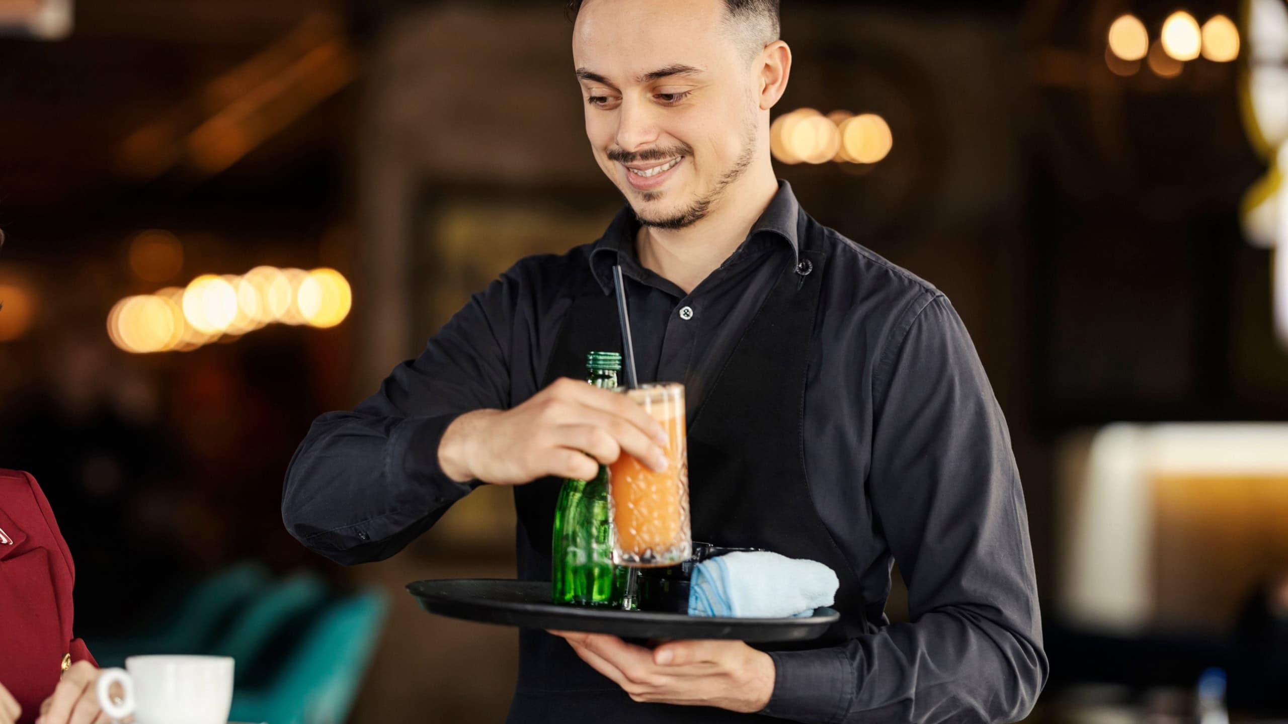 Friendly waiter is bringing refreshment on a tray to a customer in a bar.