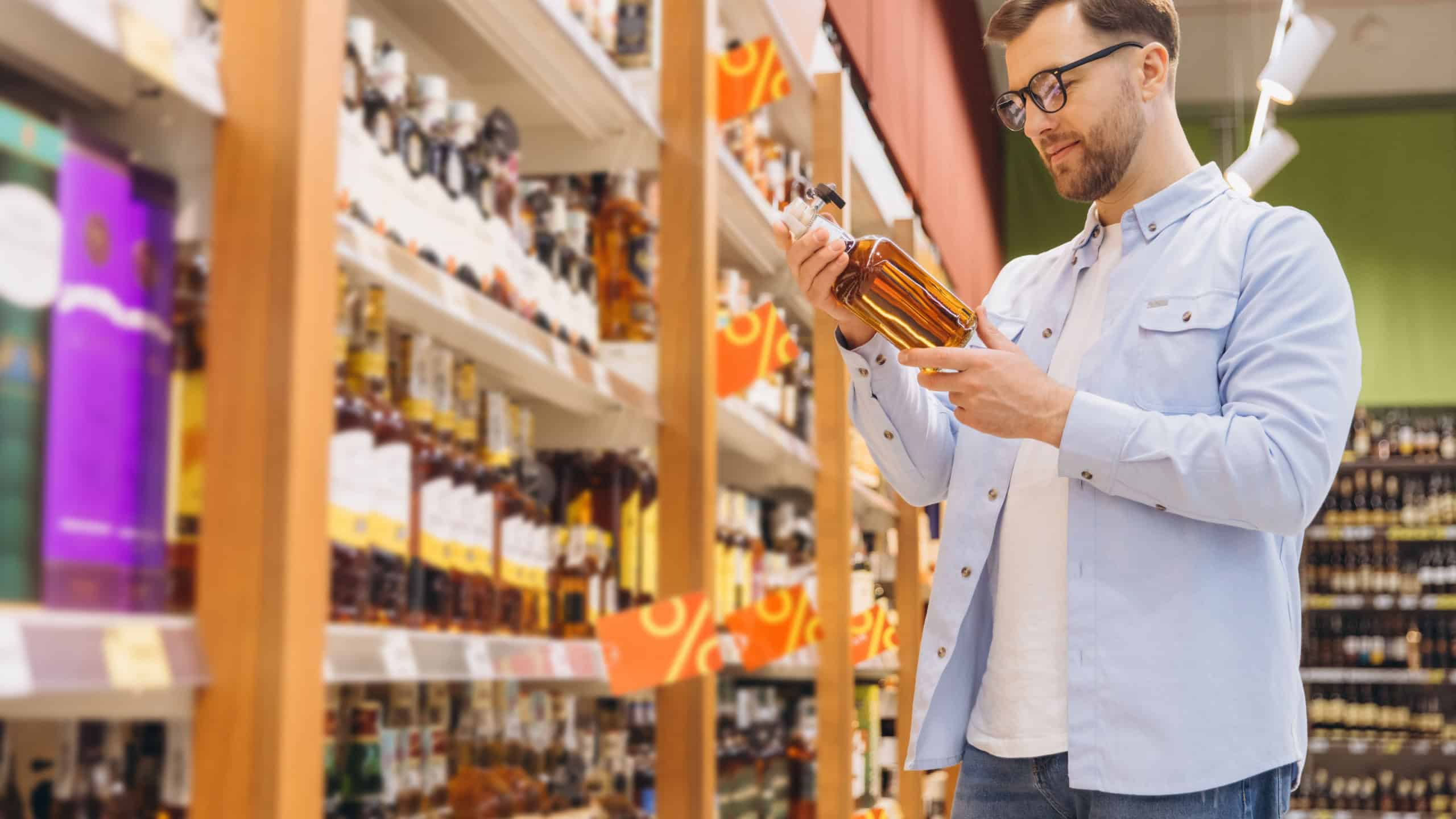 Man reading label of liquor bottle while shopping in grocery store