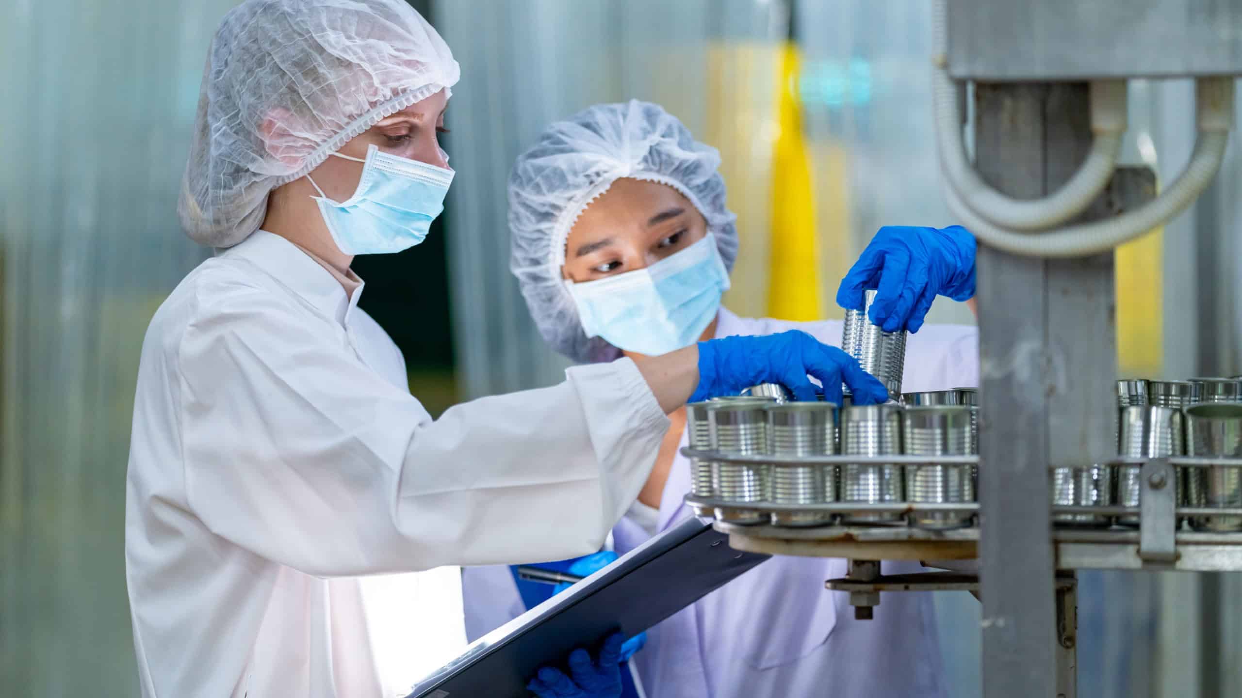 Canned food manufacturing factory industry entrepreneur. Quality control officer inspecting and sampling in production line. Processed food packed in aluminum cans move along automated conveyor belt.