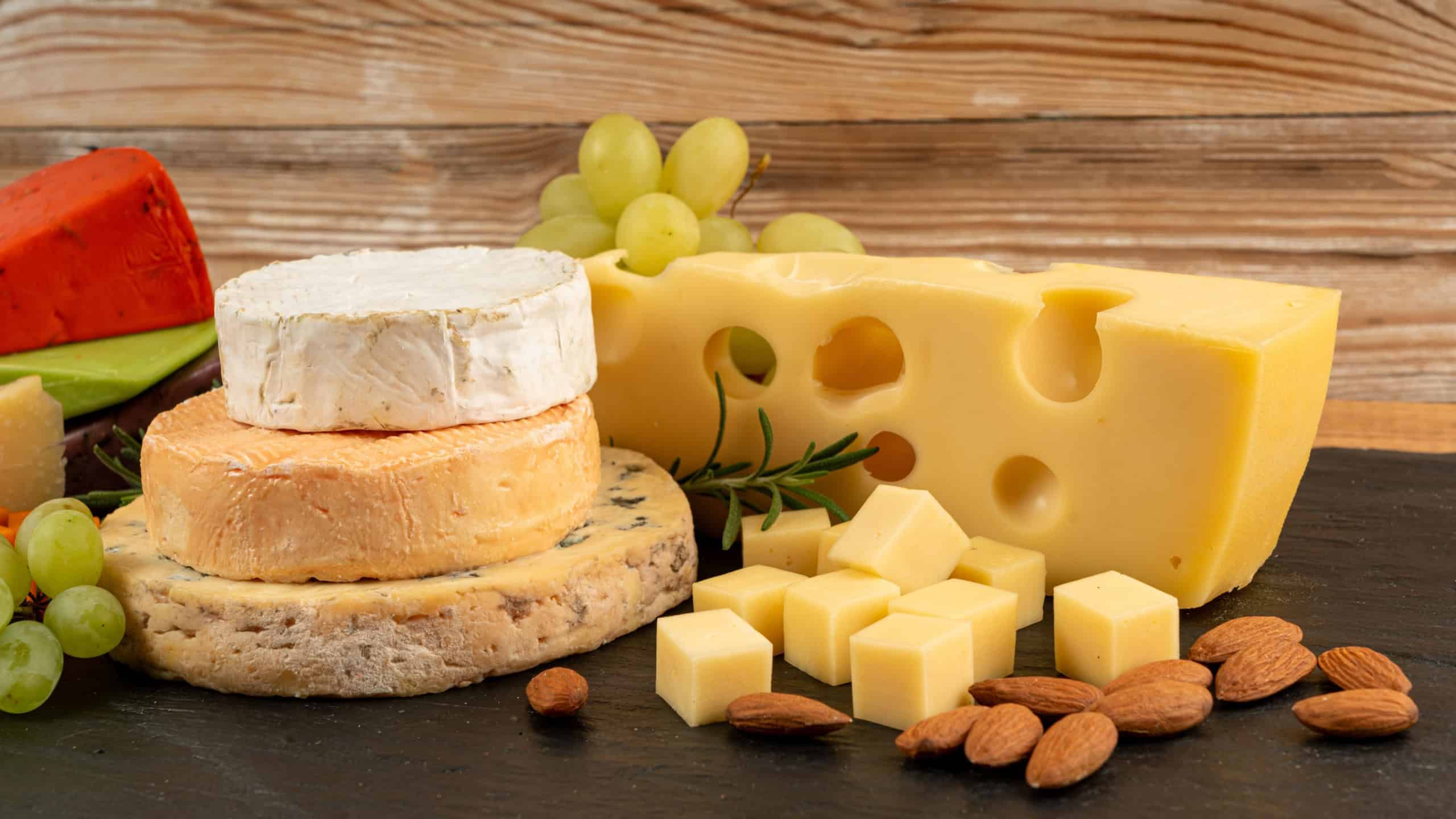 Cheese plate of color cheeses variety, yellow, white and blue gorgonzola platter, munster, fourme cheese board, assorted chopped dairy products, many stinky French cheeses on wood