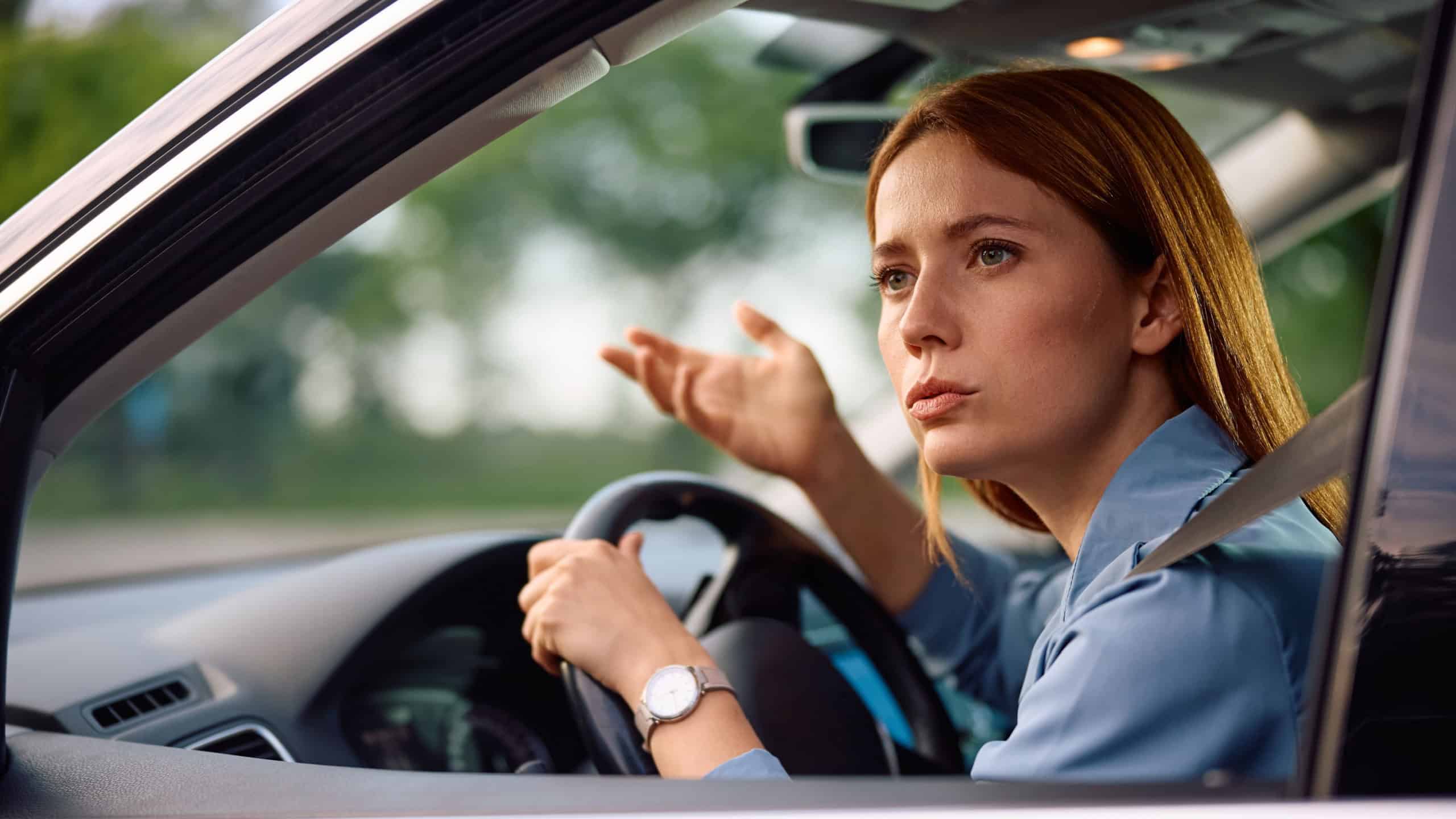 Businesswoman feeling upset while driving and looking through the side window of a car.