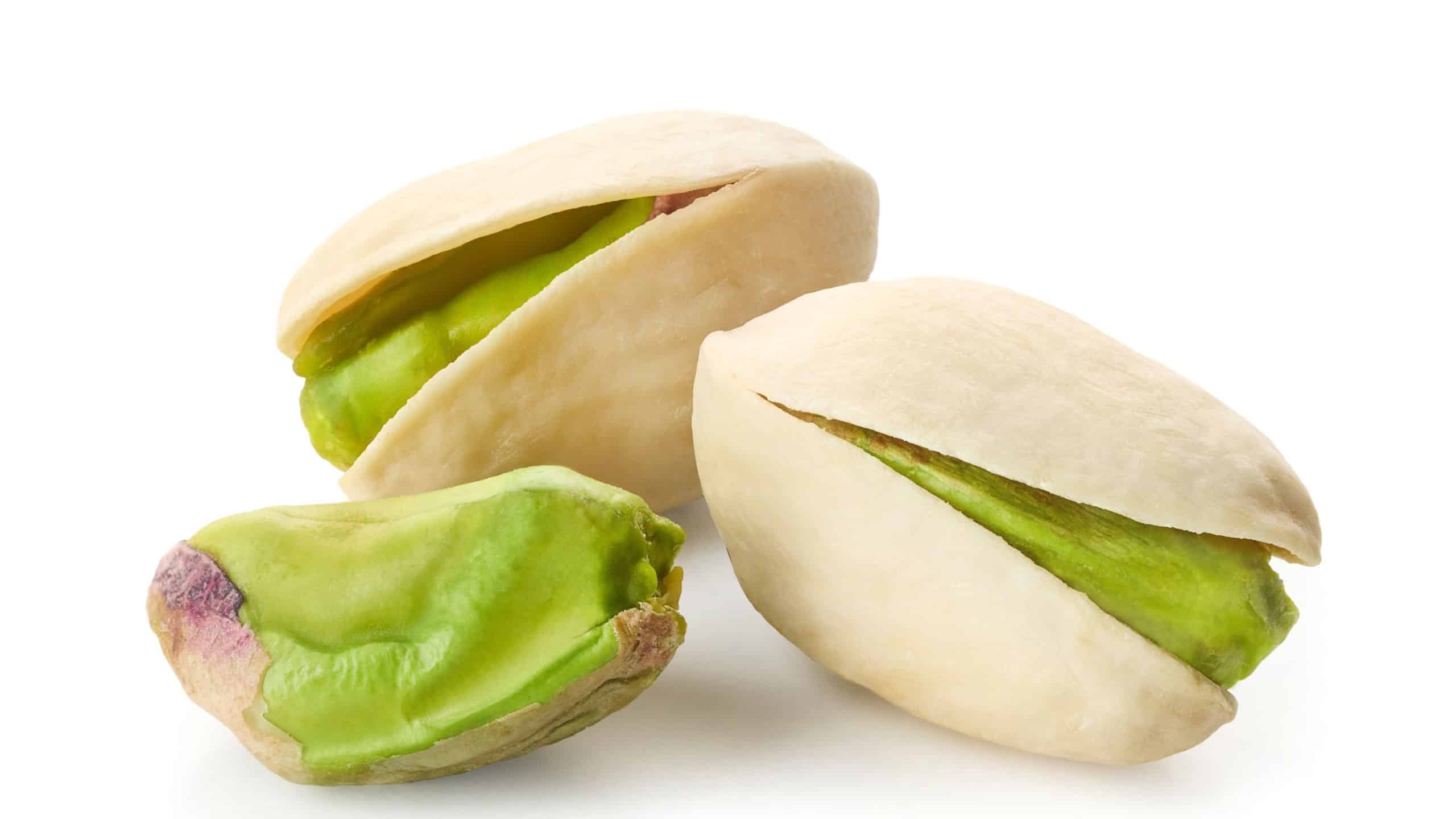 Close-up of three green unpeeled pistachios isolated on white background