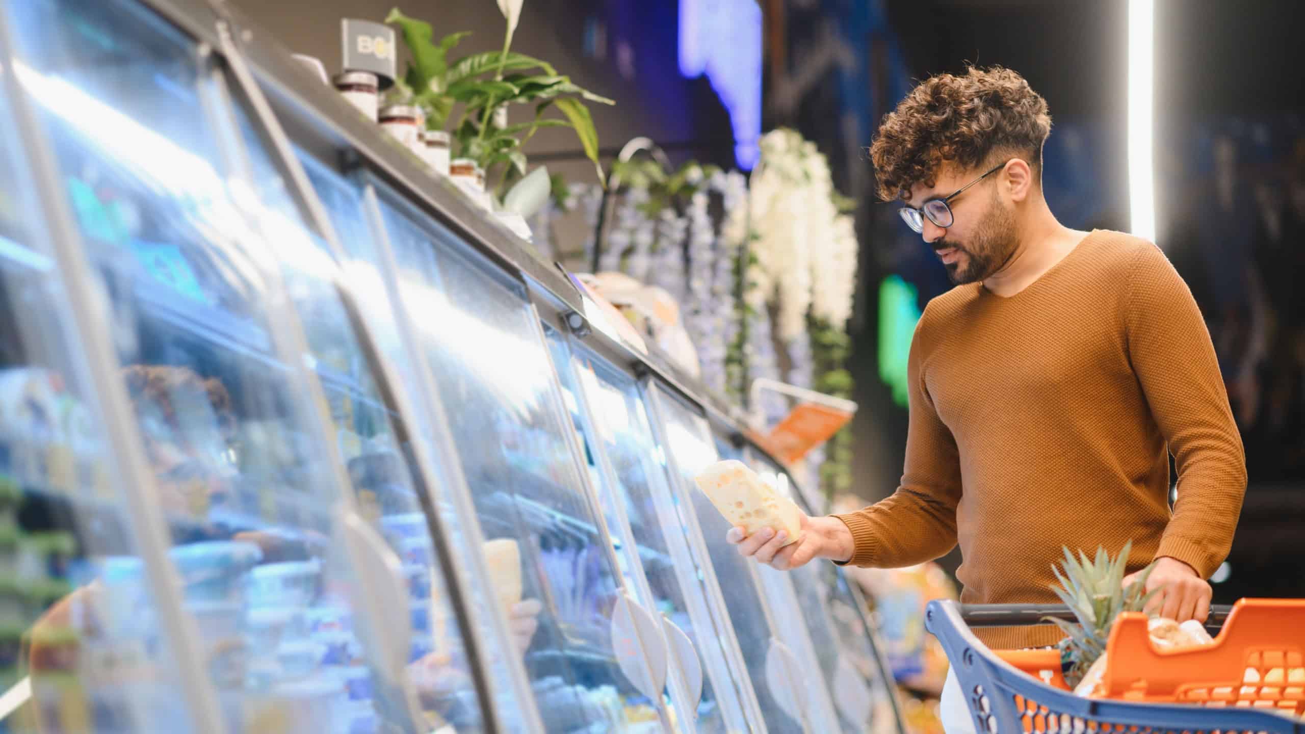 Customer buying groceries, shopping in supermarket, choosing frozen food from refrigerator, pushing shopping cart