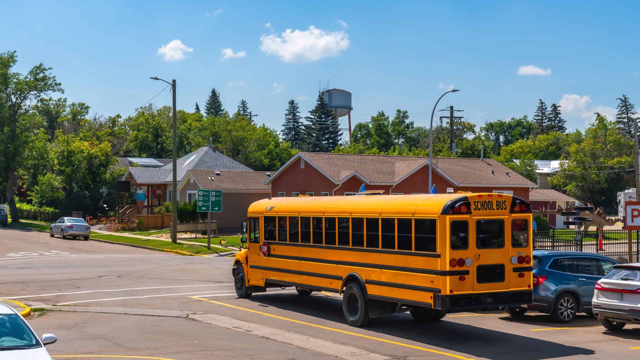 Classic yellow school bus driving away from an intersection in a quiet residential area, marking the end of the school day under a clear blue sky