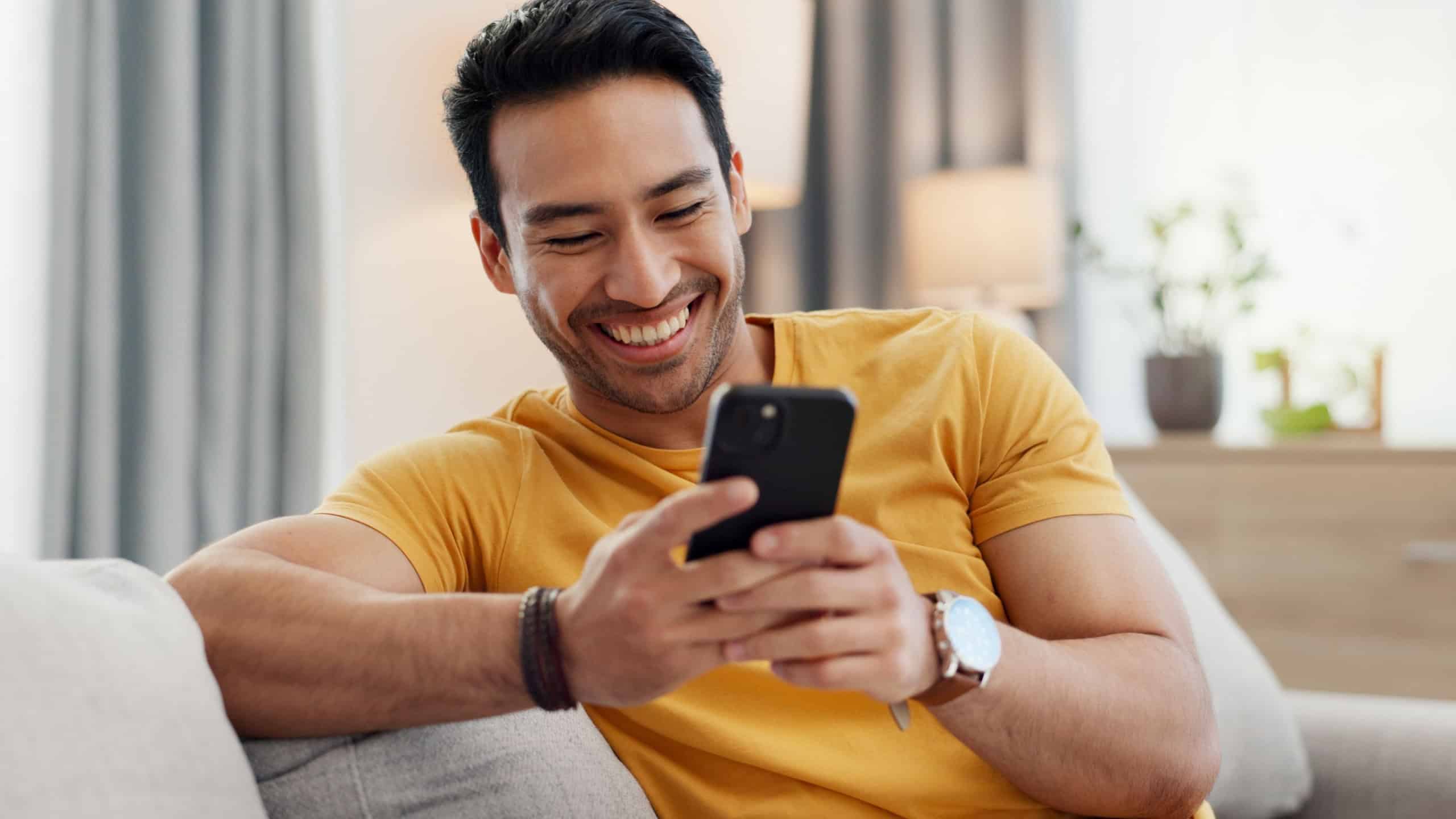 Mobile, relax and happy man in home for internet, social media post and reading news. Cellphone, living room and person with app for online text, communication and check message with notification