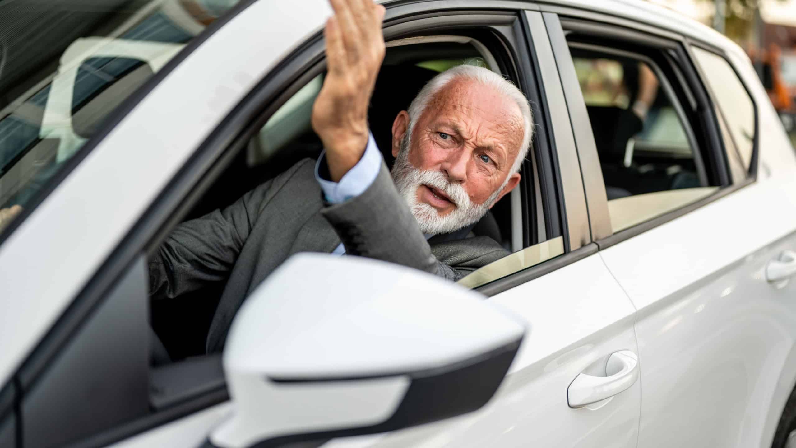 Upset mature executive gesturing and arguing while driving through city streets, expressing frustration and stress during a traffic jam