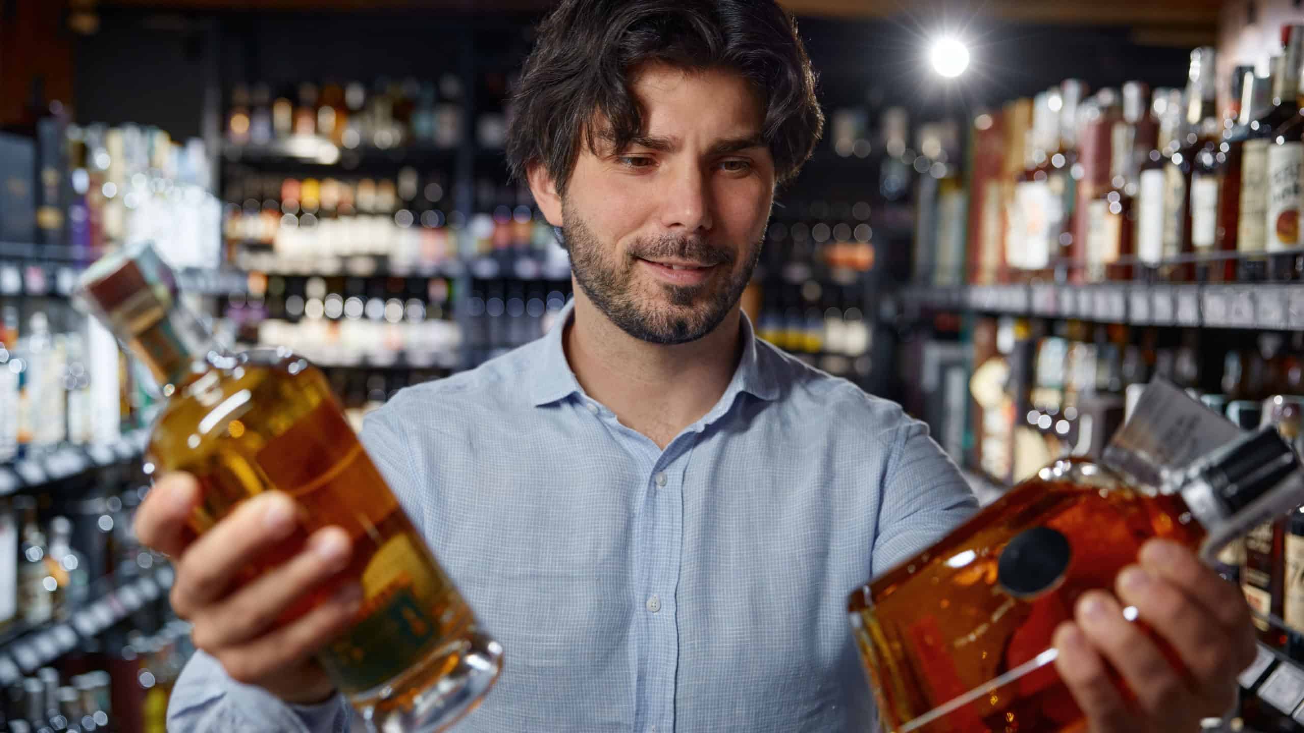 A man holds two bottles of alcohol in a liquor store