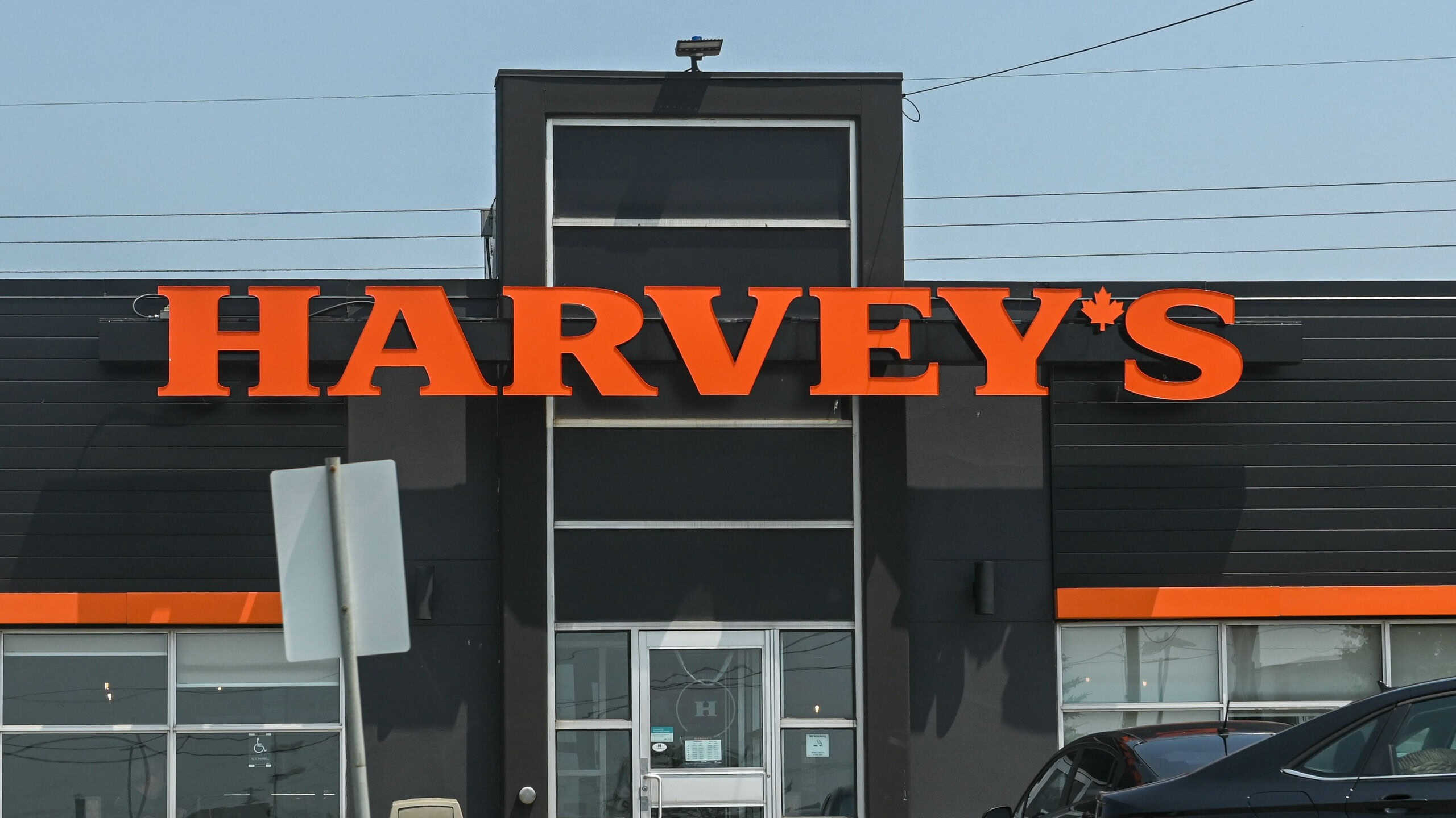 A Harvey's fast-food restaurant sign is mounted on a pole in a parking lot on a sunny day