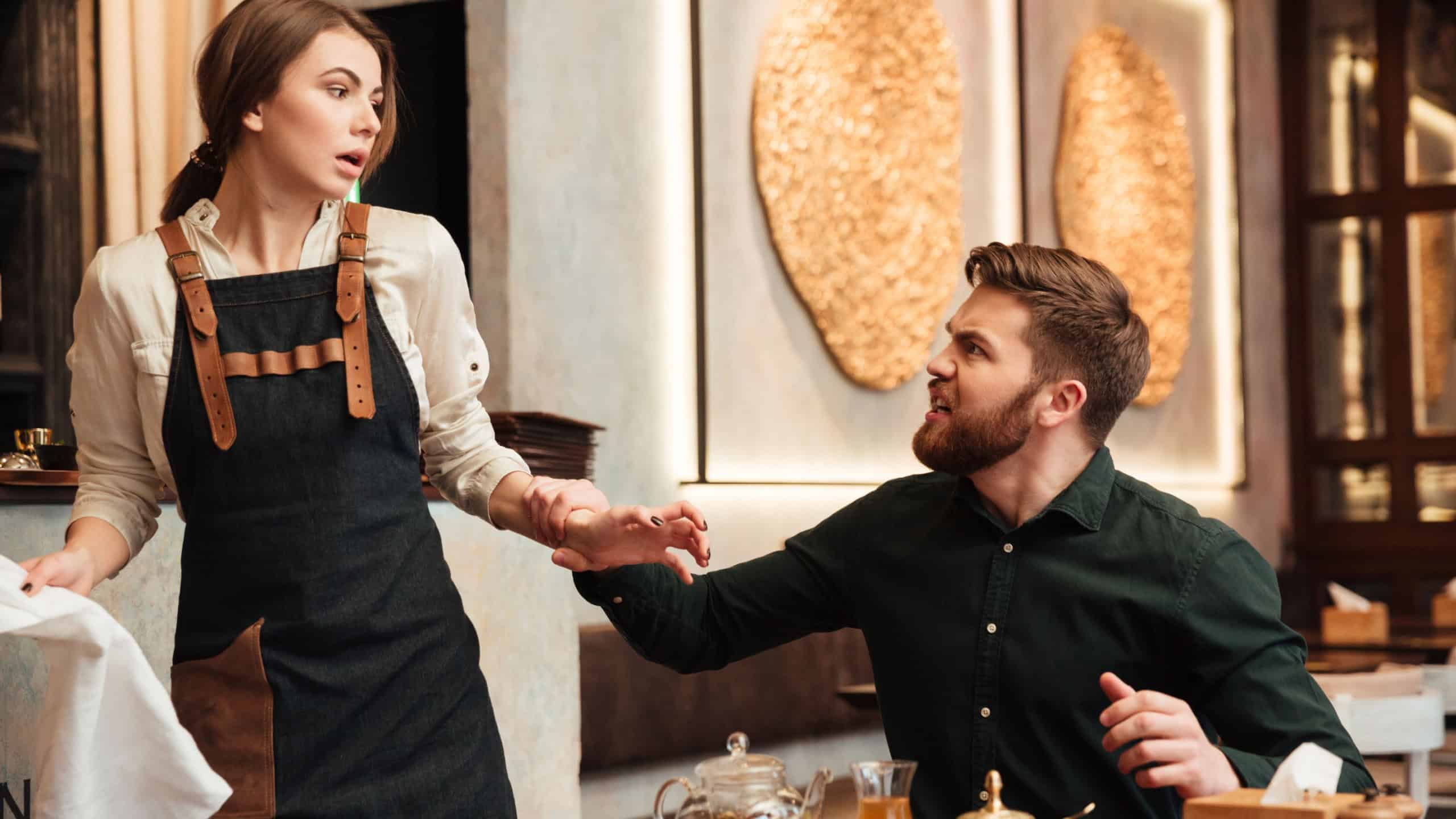 Photo of angry screaming bearded young man sitting in cafe. Looking at waiter.