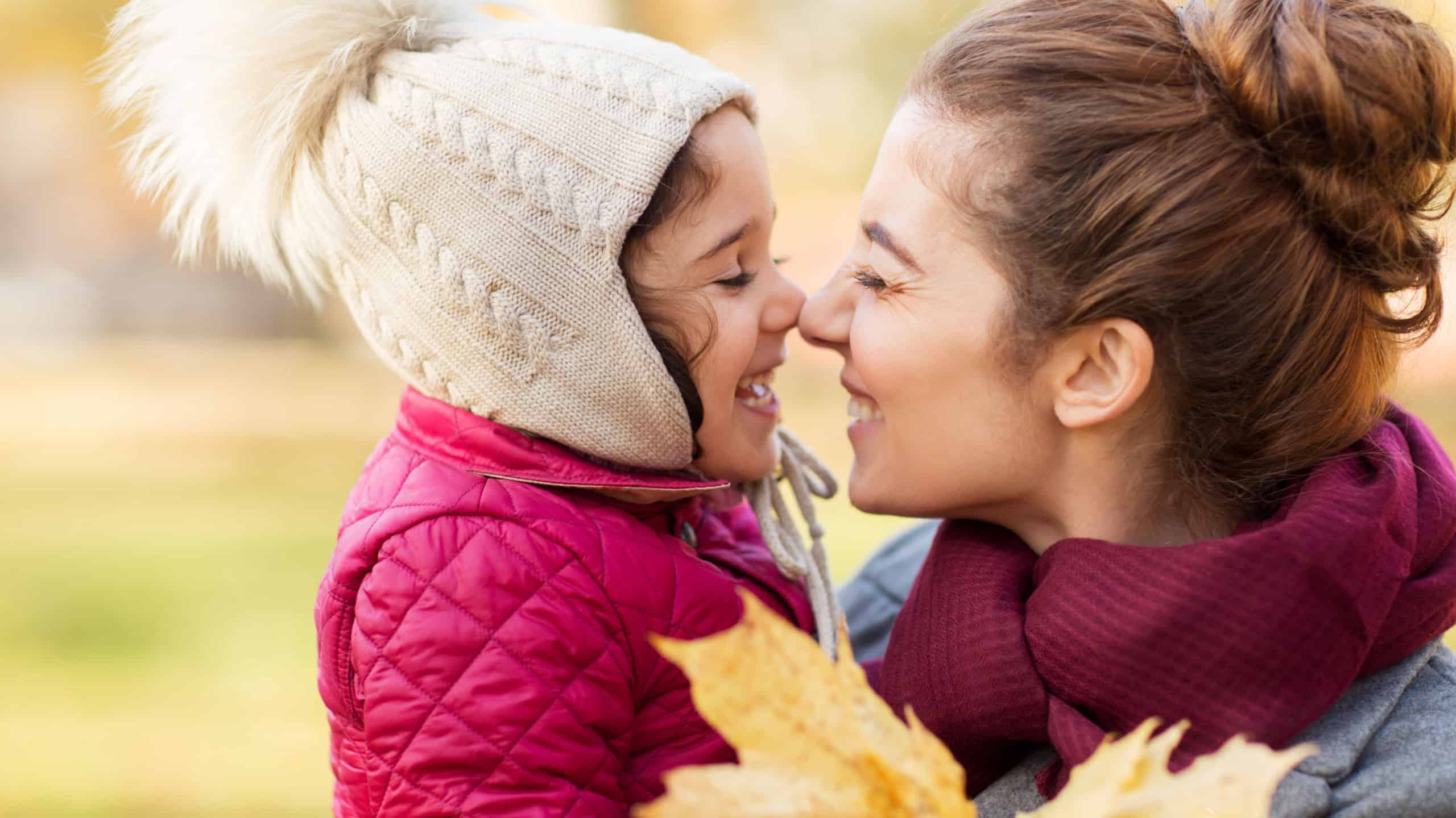 Family, love and people concept - happy mother and little daughter with autumn maple leaves rubbing noses