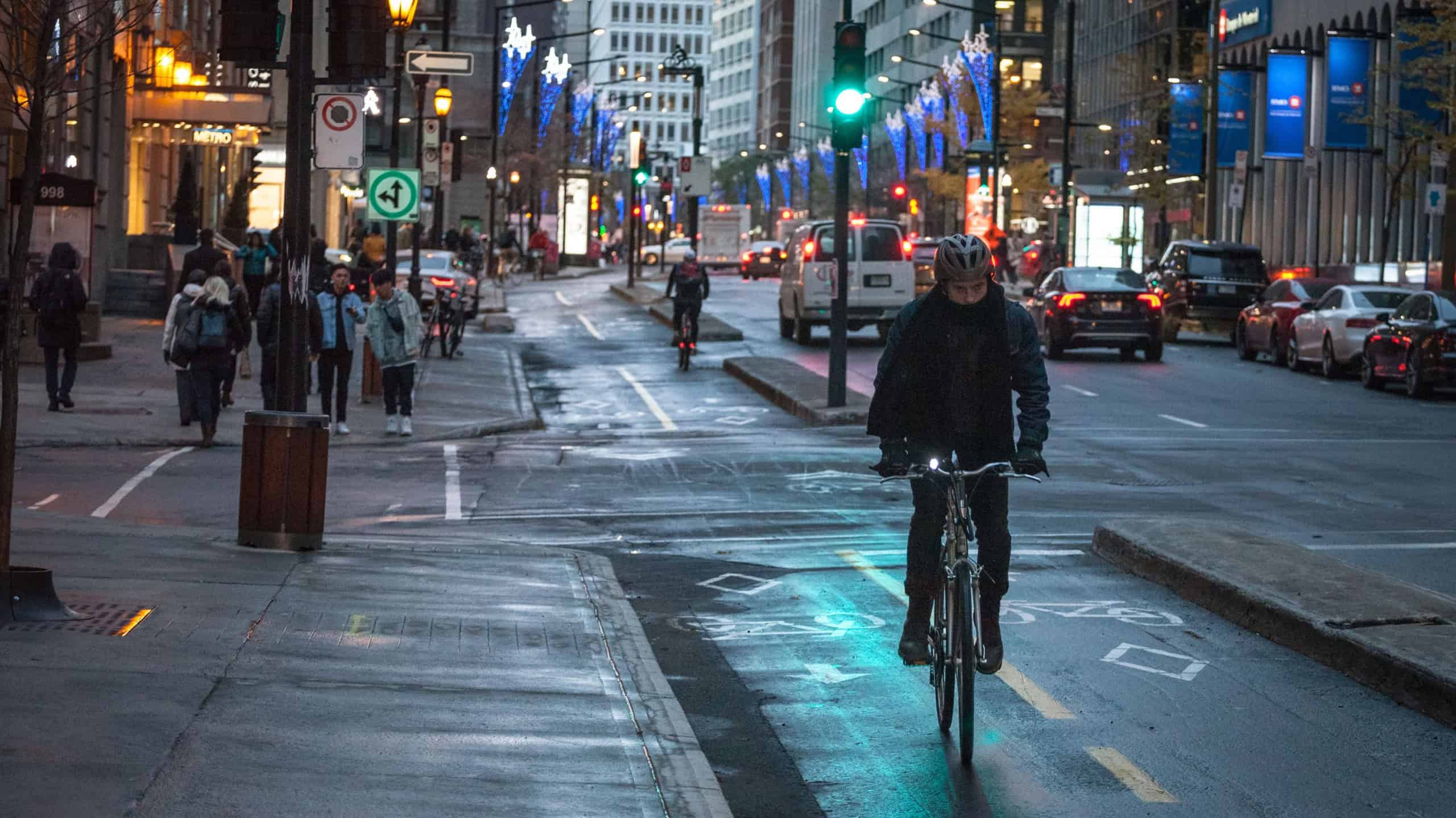 Cyclist, delivery courrier guy, standing with his bicycle on a bicycle lane in downtown center business district at night, in Montreal, Quebec