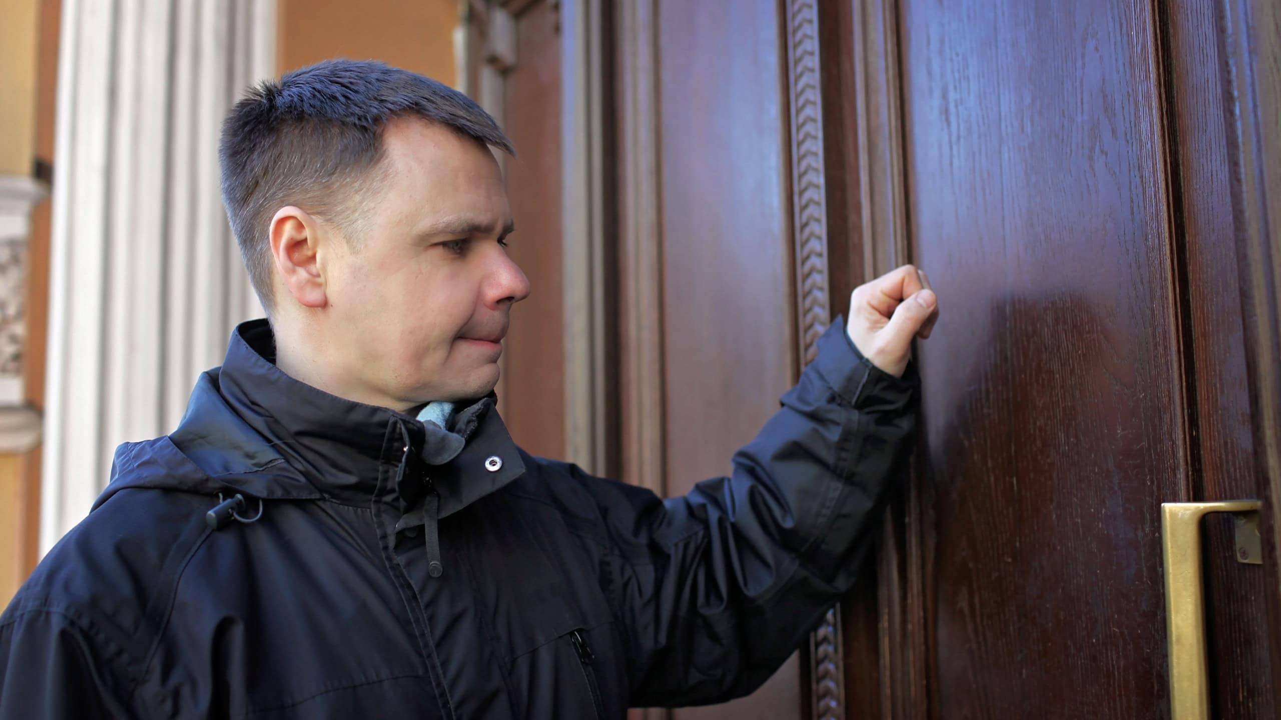 Middle-aged man waiting in front of wooden house door and thinking to knock or not to knock, people relationship, date and meeting concept, outdoor