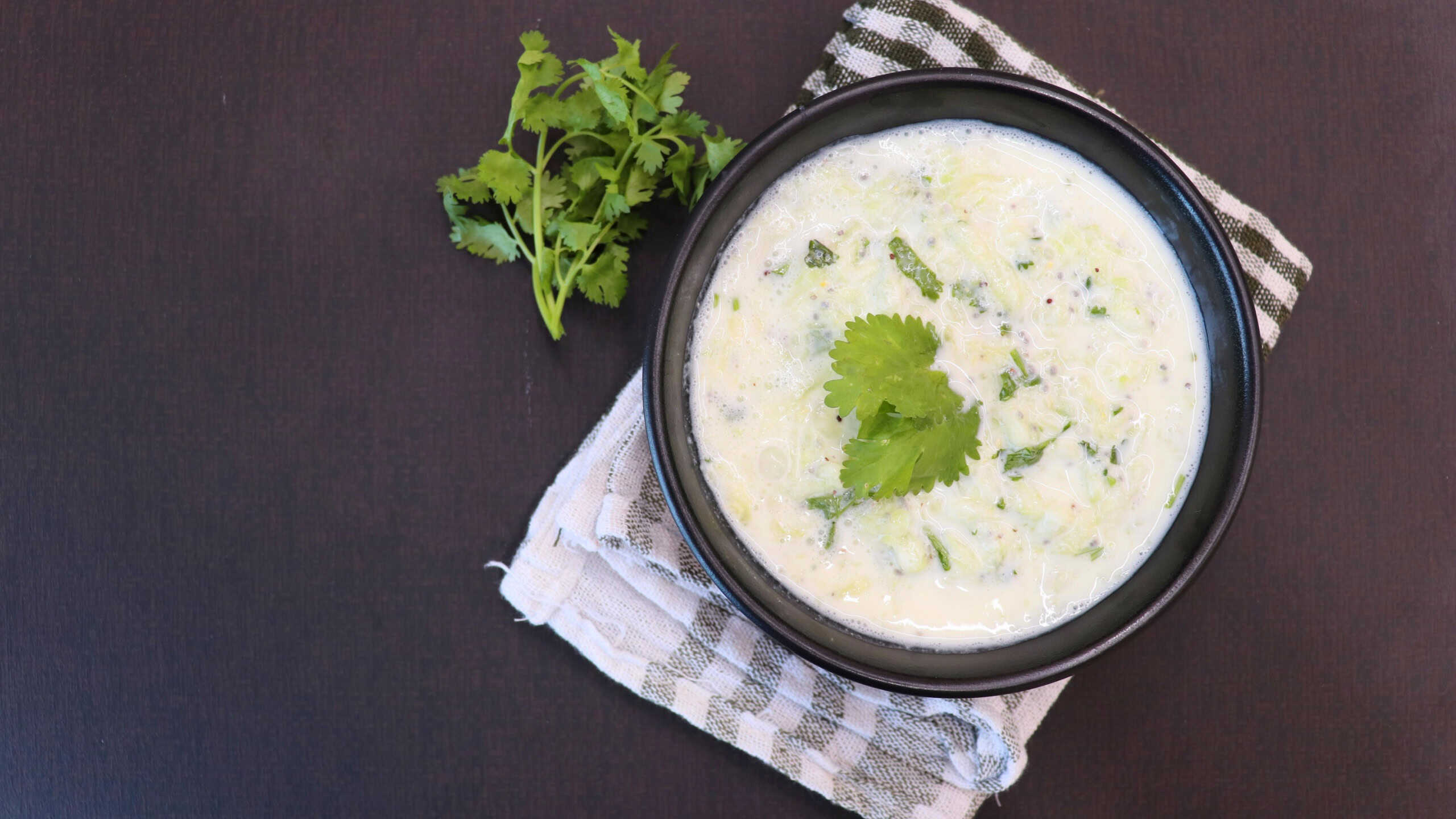 Indian Fresh sauce called Raita with herbs, curd and grated cucumber close-up in a bowl on the table. with some saute vegetables like green bell papers and fresh green peas