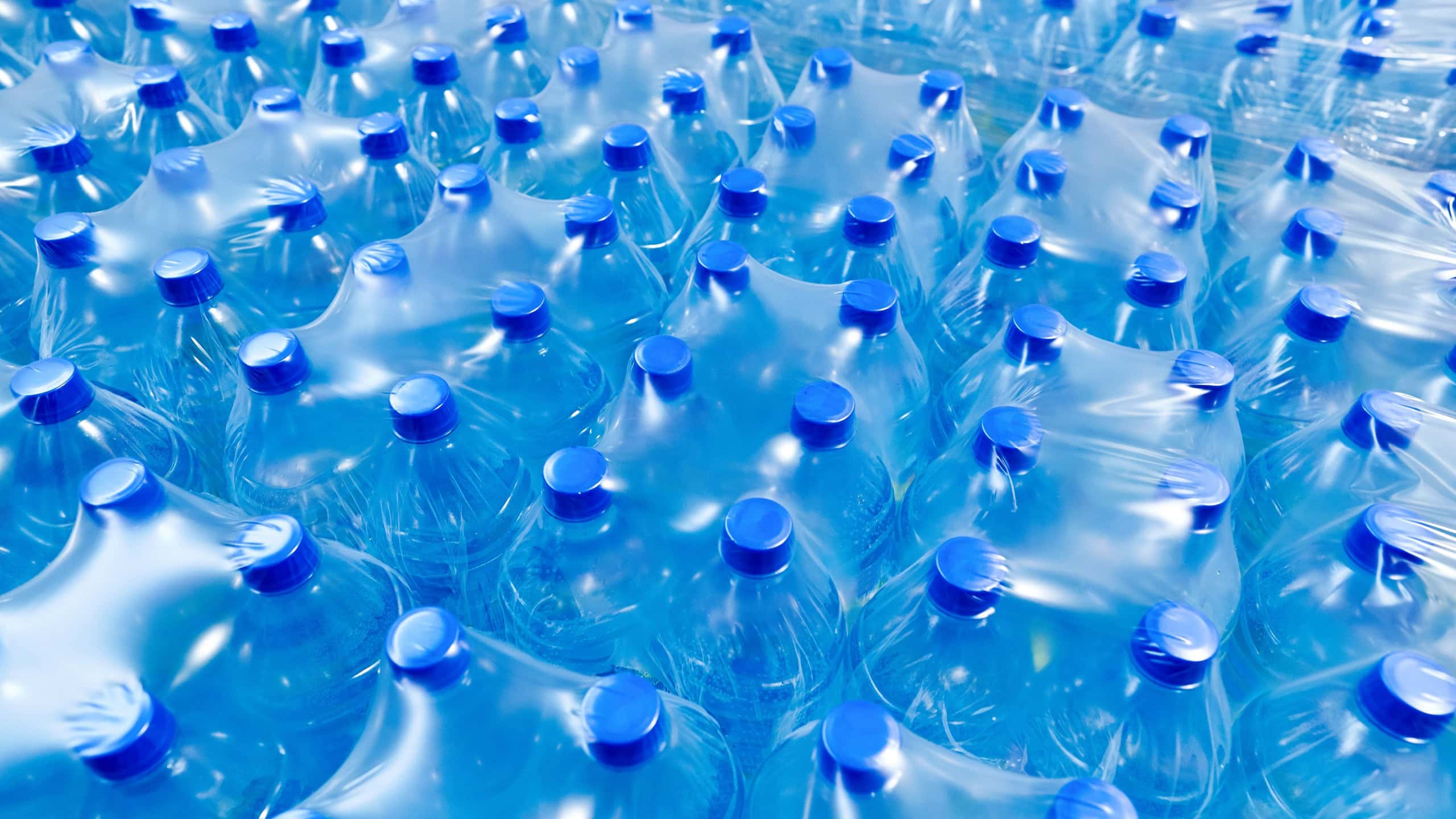 A lot of plastic bottles with blue caps with clean drinking water in a supermarket. Packed in plastic wrap.