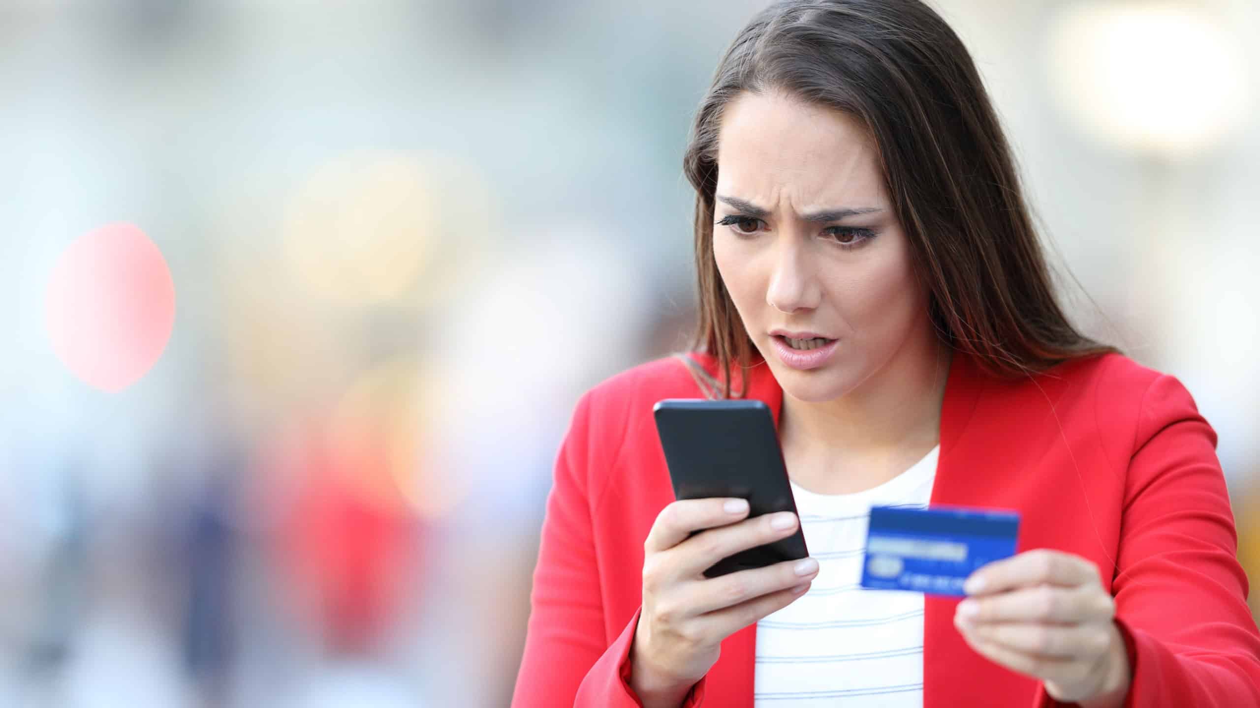 Worried woman holding gift card looking at smart phone in the street