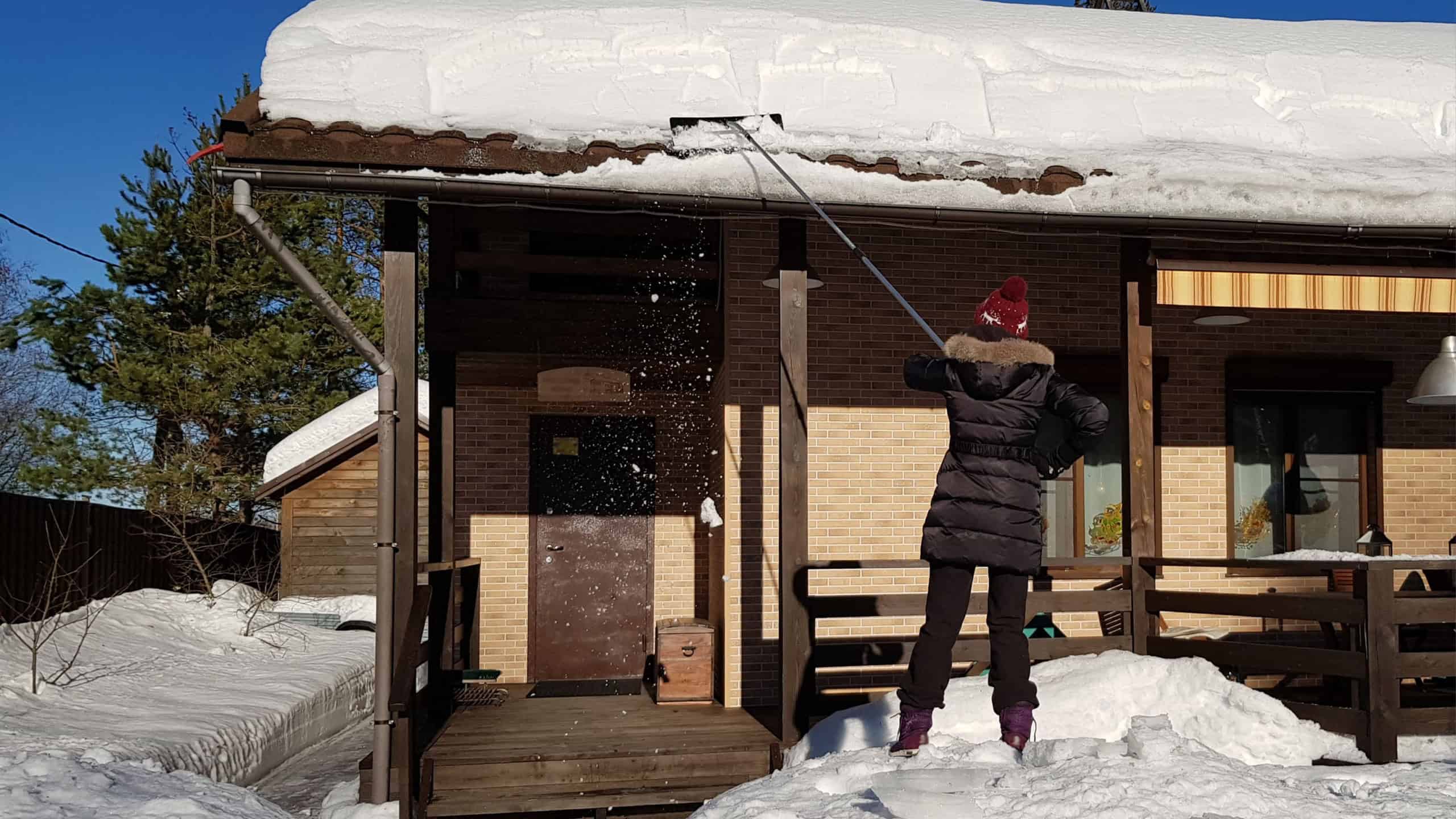 Woman cleans snow with shovel from roof of house, apartment building on clear winter frosty day, St. Petersburg, Russia