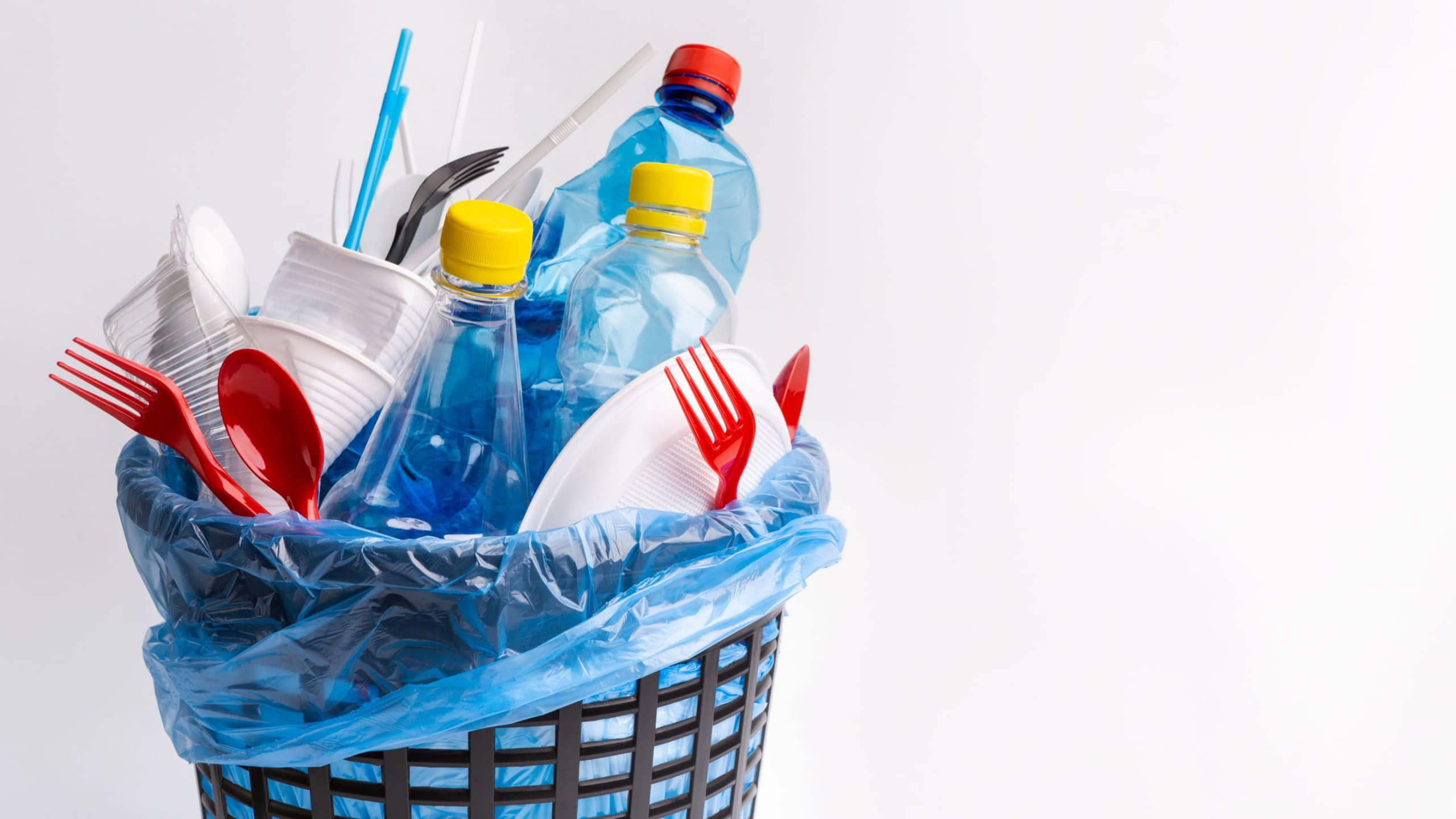 Say no to single use plastic. A black trash can with used plastic items isolated on white background
