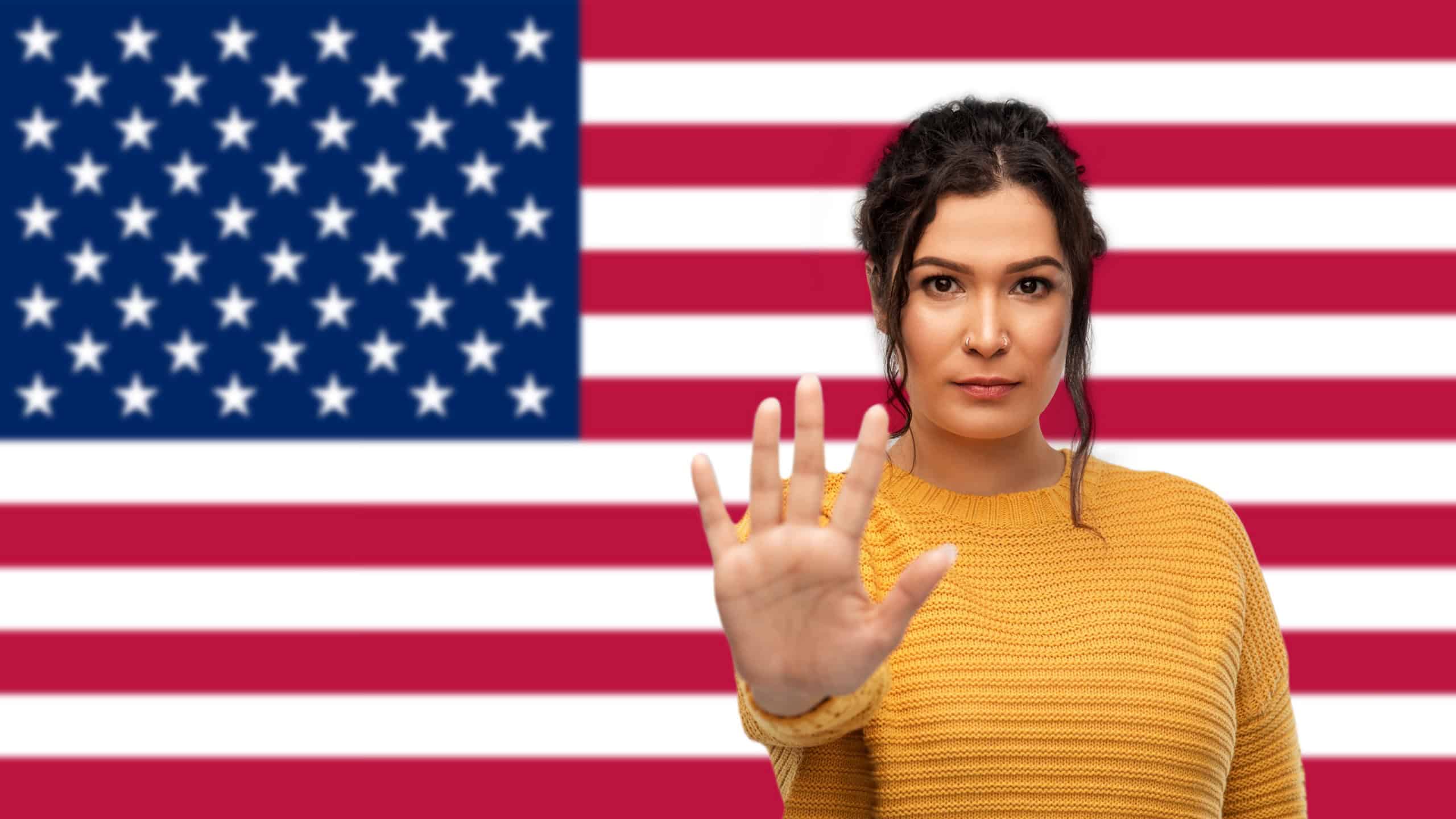 Prohibition and national concept - serious young woman showing stop gesture over flag of united states of america background