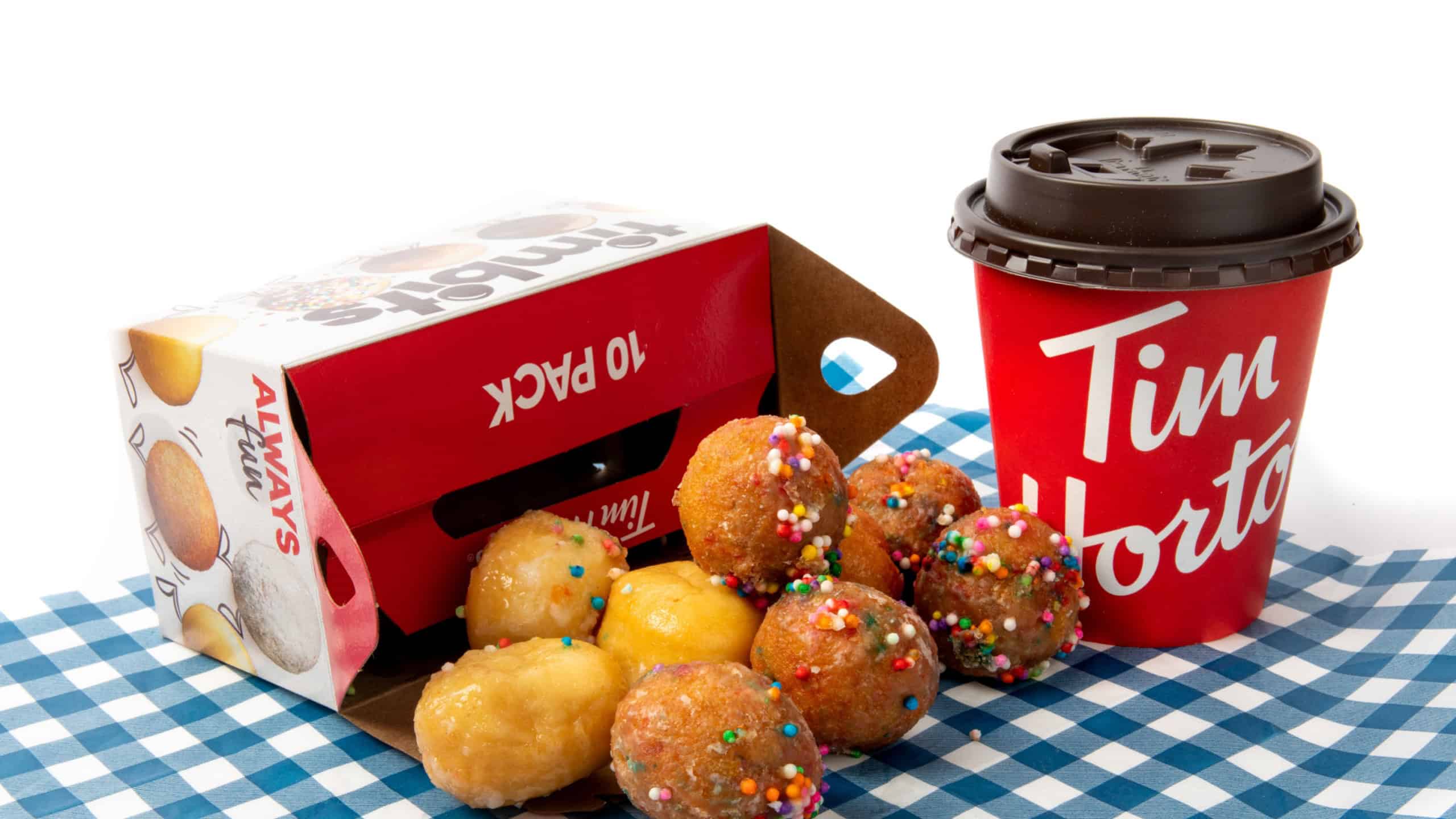 An open box of Tim Horton's Timbit doughnut holes spilled onto the table with a paper cup of Time Horton's coffee in the background