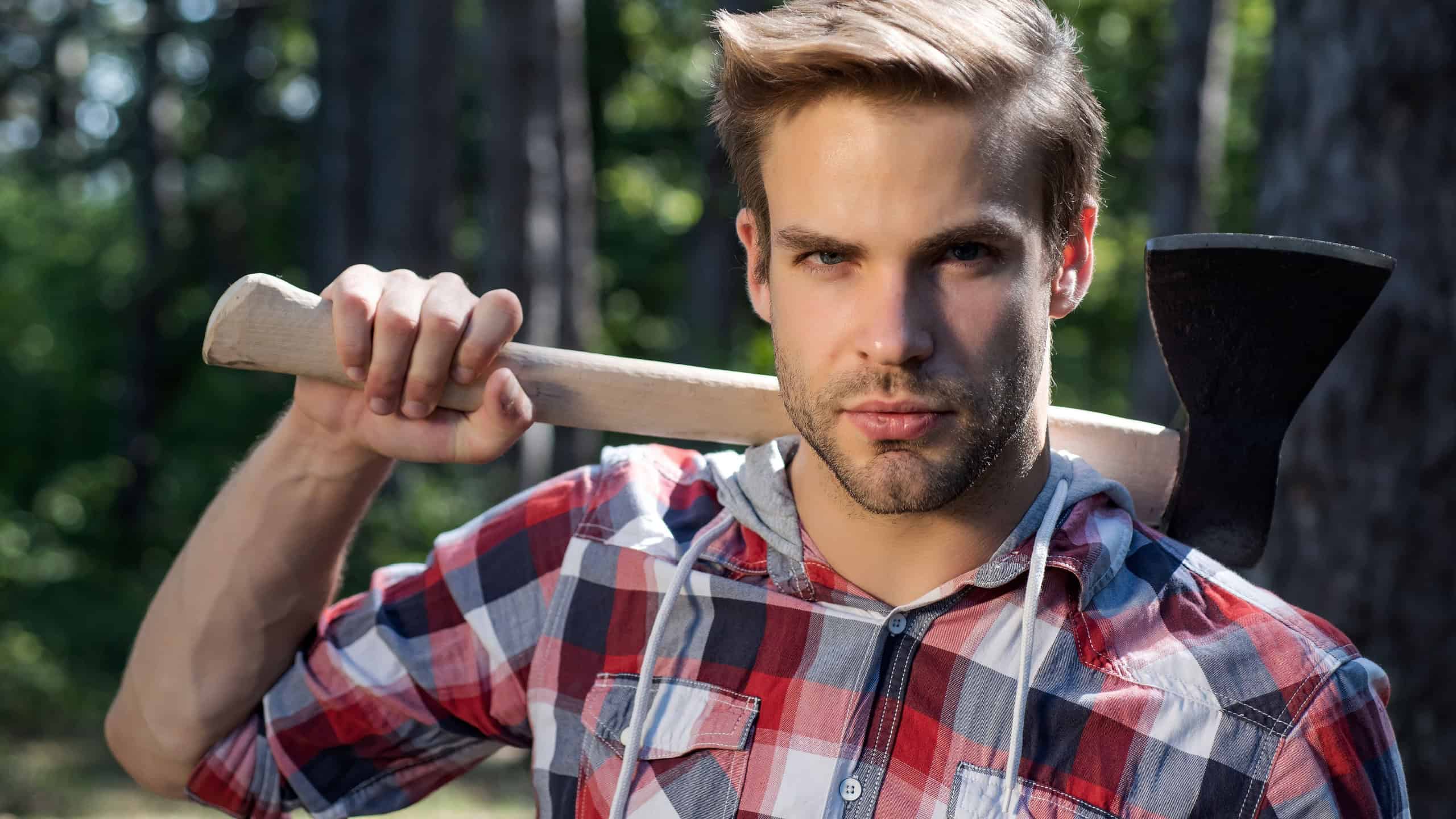Lumberjack handsome man on serious face with axe outdoor. Close up portrait of young guy woodcutter hold ax. Mens power concept