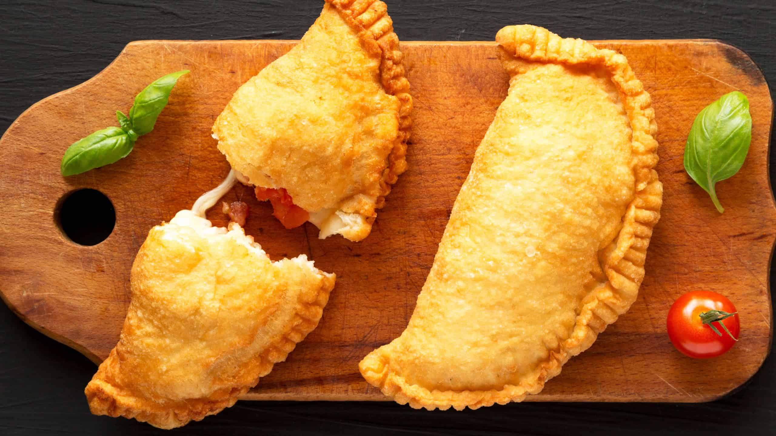 Homemade Deep Fried Italian Panzerotti Calzone with tomato and mozzarella on a rustic wooden board on a black surface, top view. Flat lay, overhead, from above.