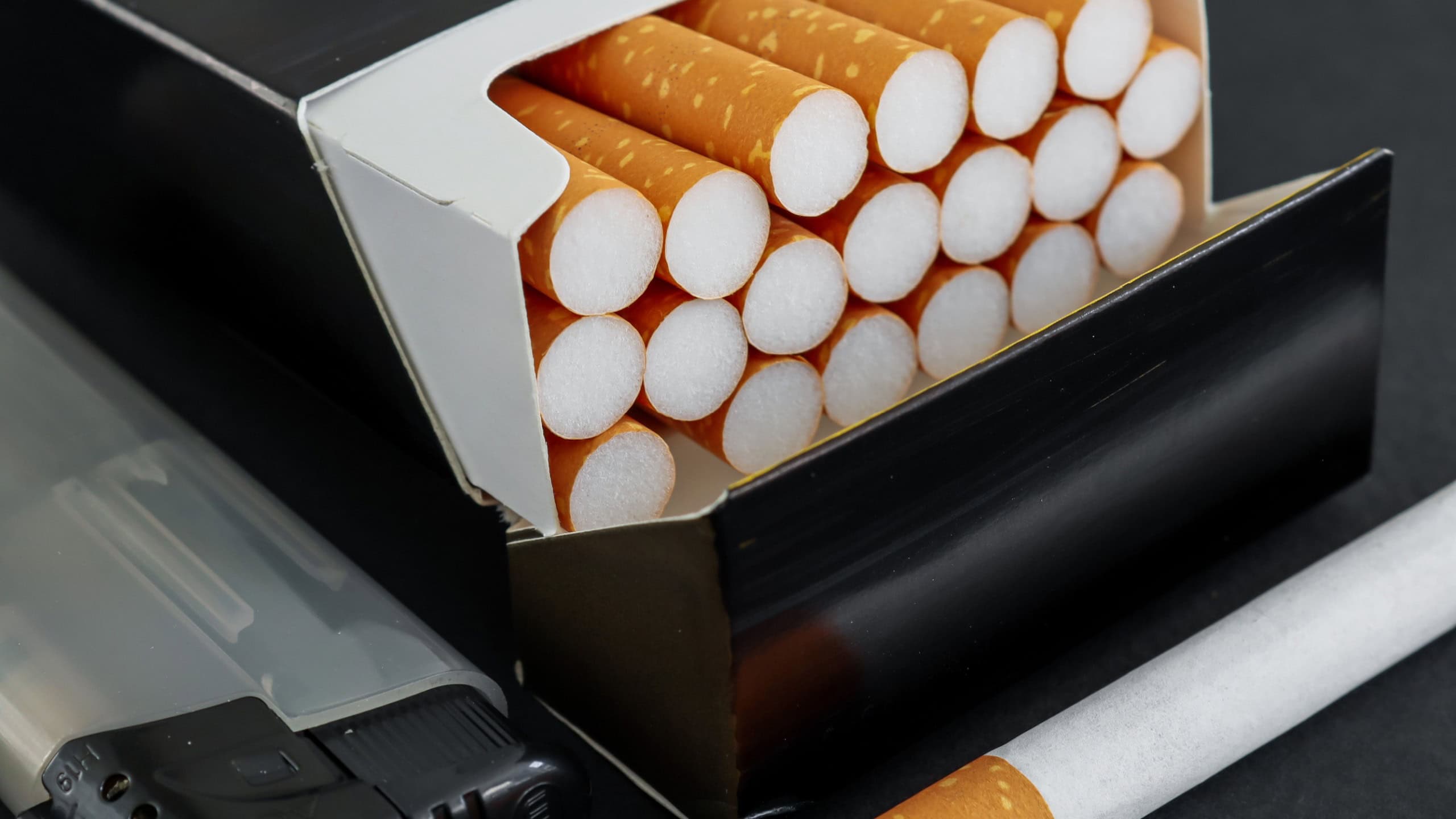 Cigarettes in a black box and a gray lighter, very close-up side view.