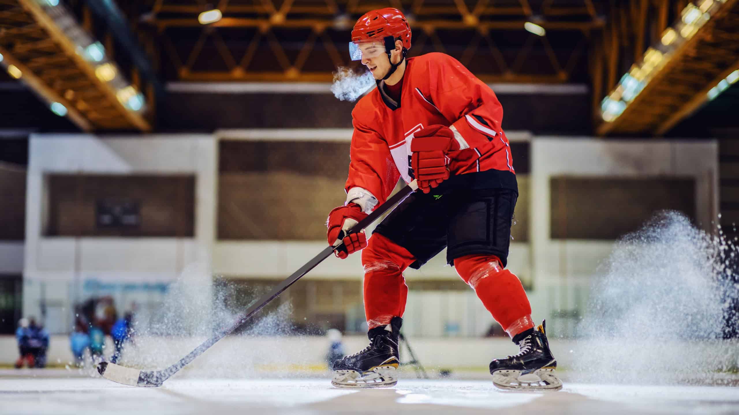 Handsome strong hockey player skating and playing important game. Hall interior. Winter sports.